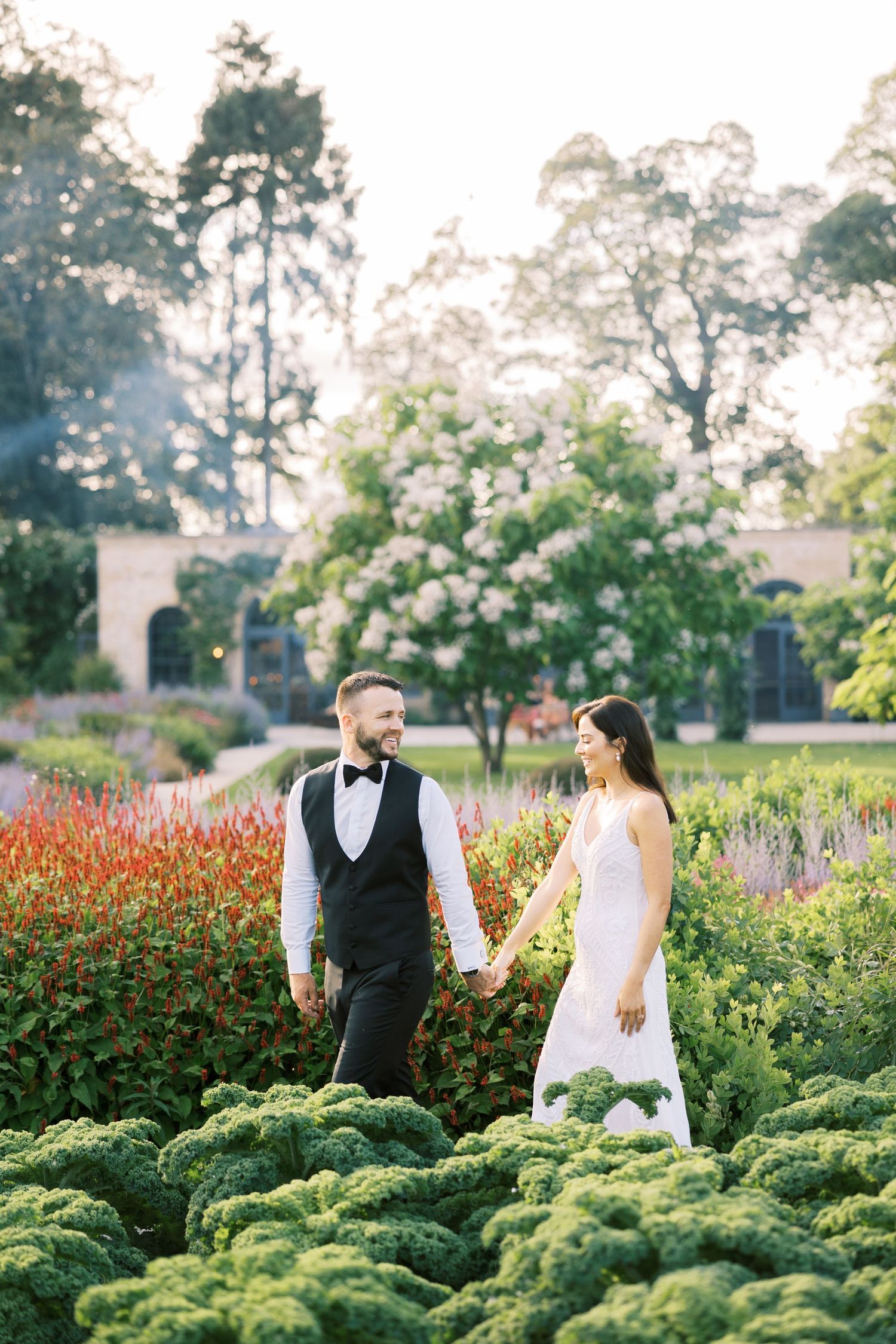 Bride and groom holding hands in a lush garden with colorful flowers on their wedding day.