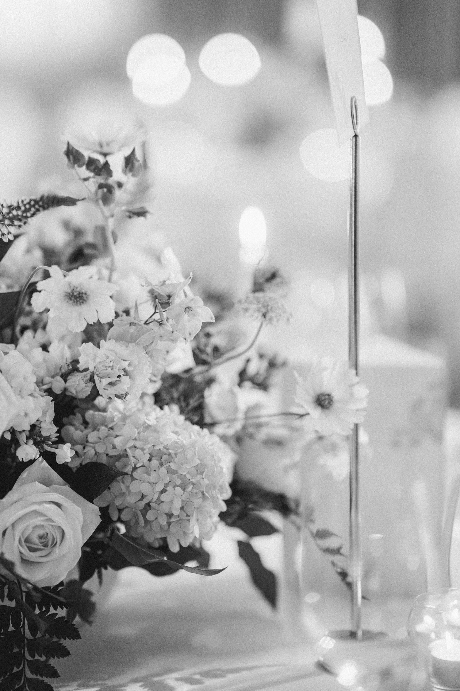 Black and white wedding table centerpiece with roses, hydrangeas, and mixed blooms beside a metal table number holder.
