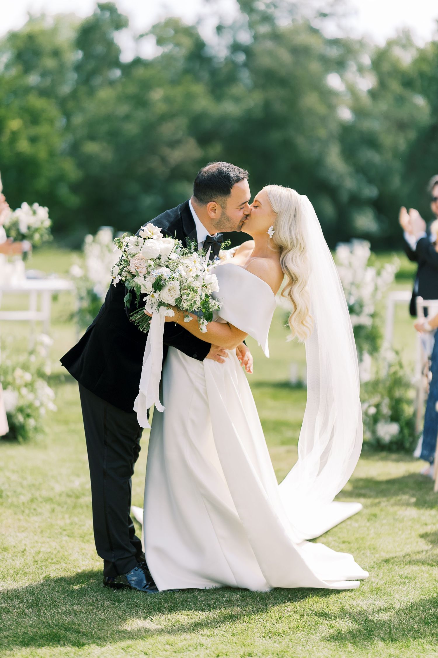 Bride and groom sharing a kiss after outdoor wedding ceremony with white floral arrangements.