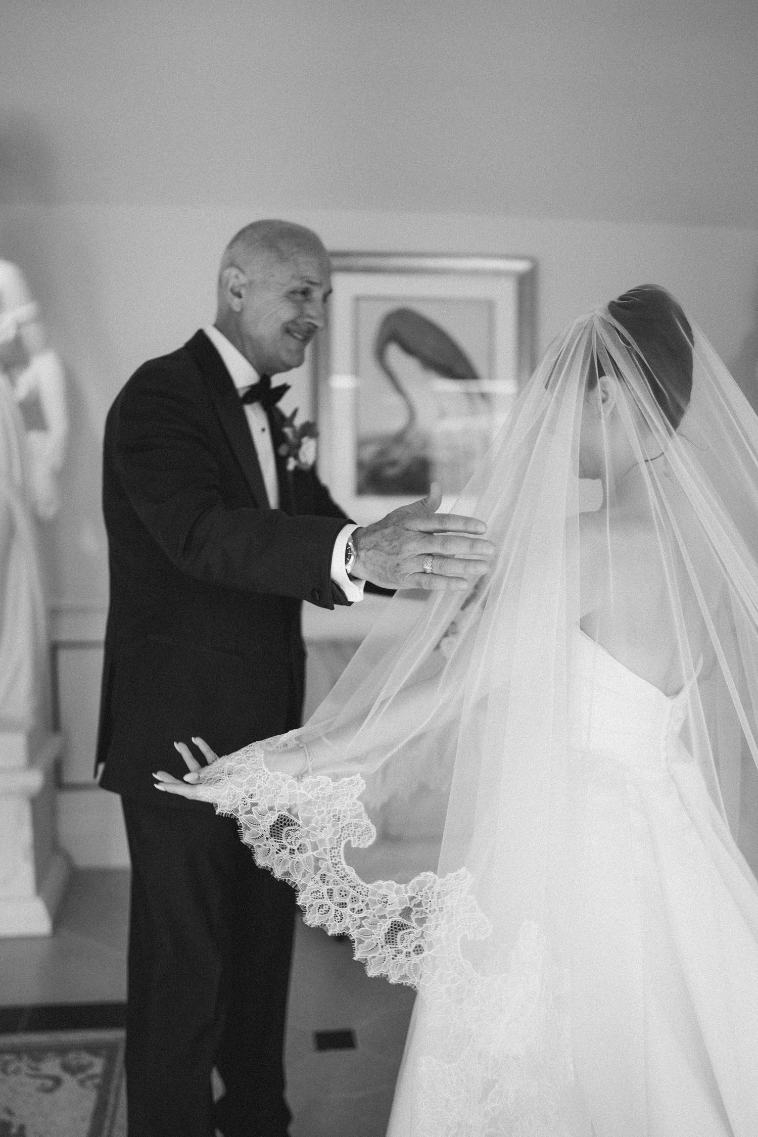 Father of bride admiring daughter in wedding dress and lace veil, black and white photo.