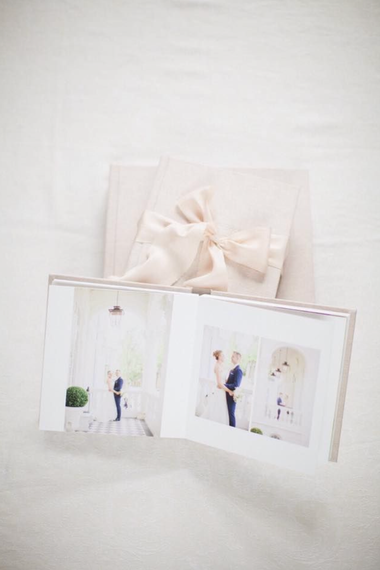 Open wedding photo album displaying couple portraits beside an elegant gift box tied with a satin ribbon bow.