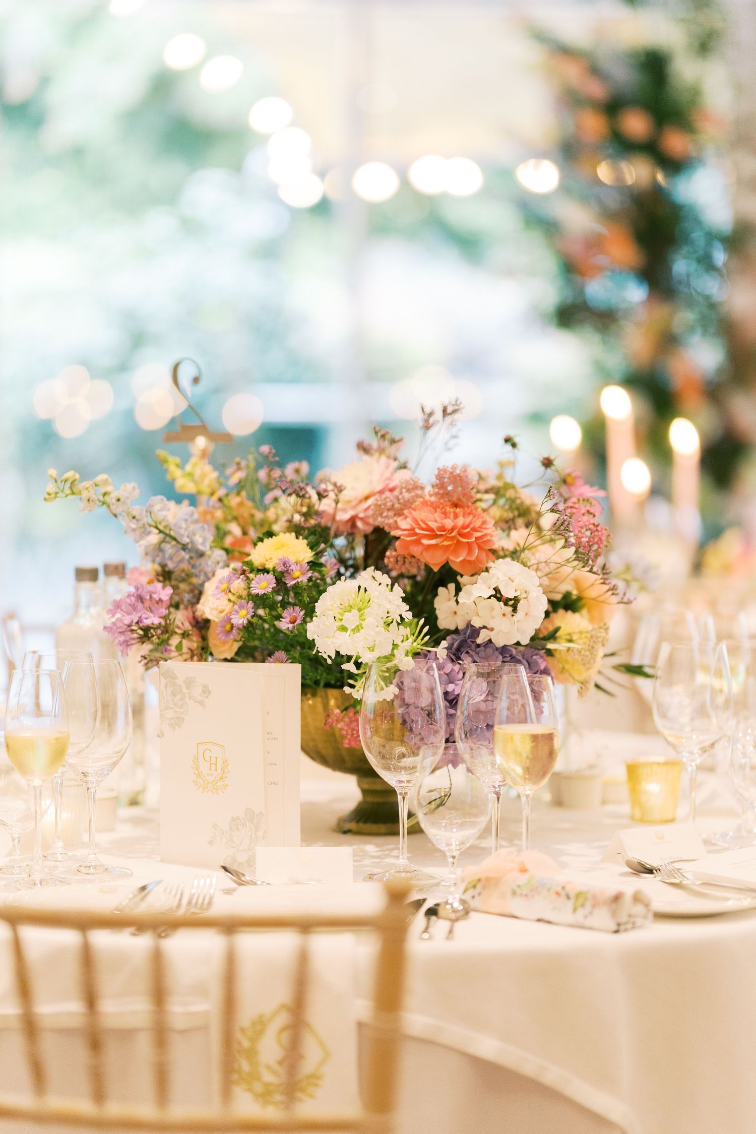 Elegant wedding reception table with colorful floral centerpiece, gold chairs, and crystal glassware.
