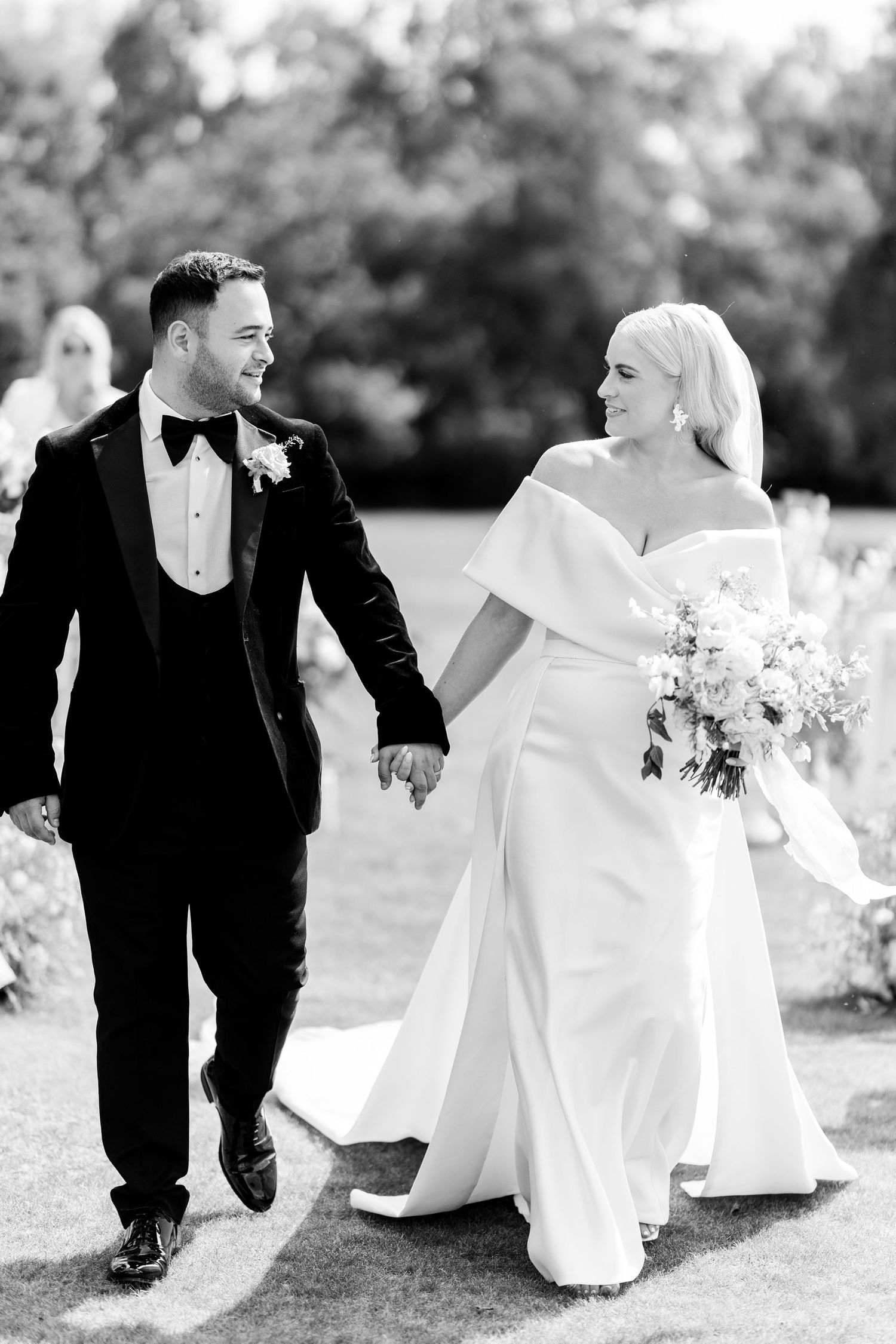 Bride and groom walking hand in hand after outdoor wedding ceremony in black and white photo.