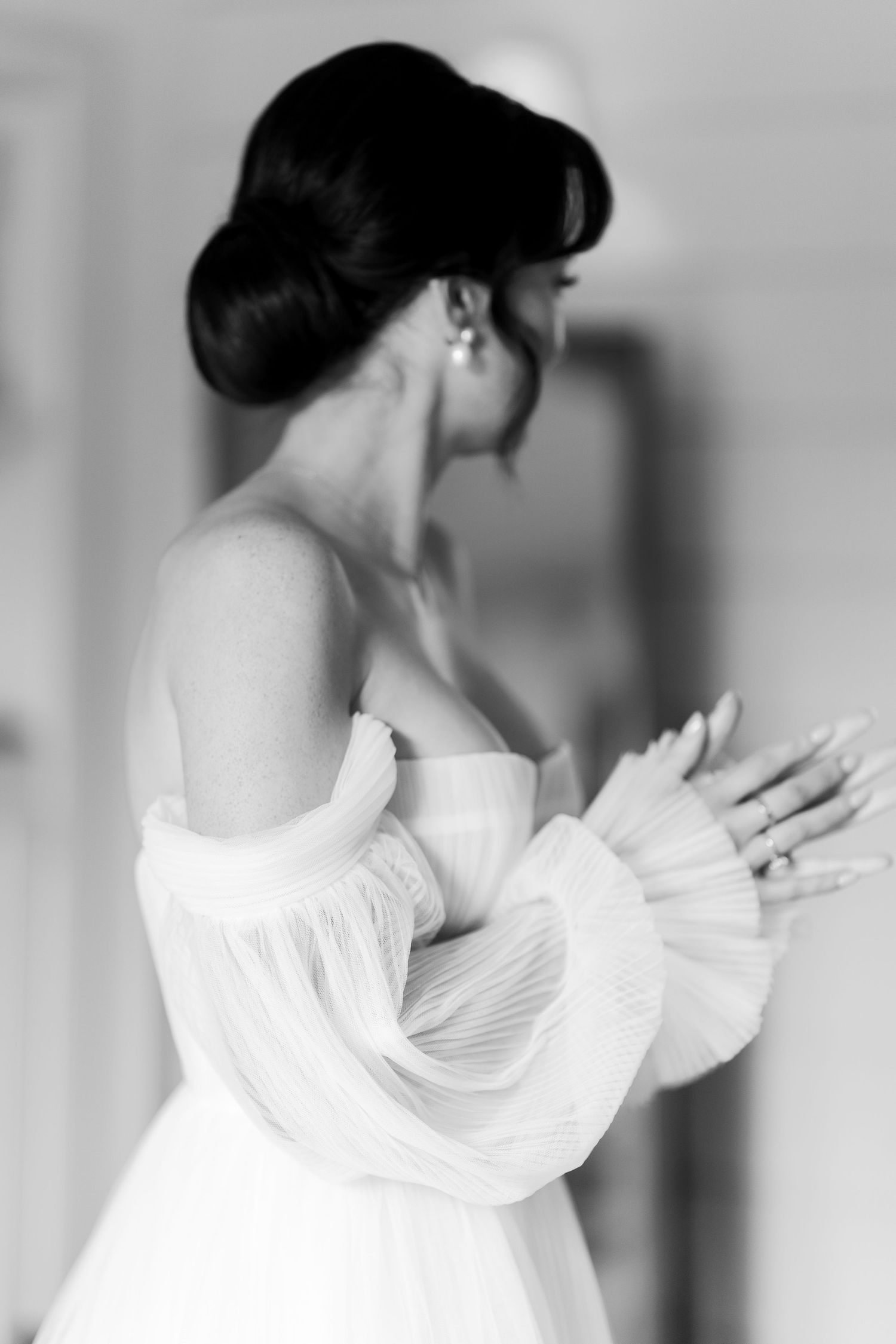 Black and white portrait of bride in strapless gown with dramatic sleeves and updo hairstyle.
