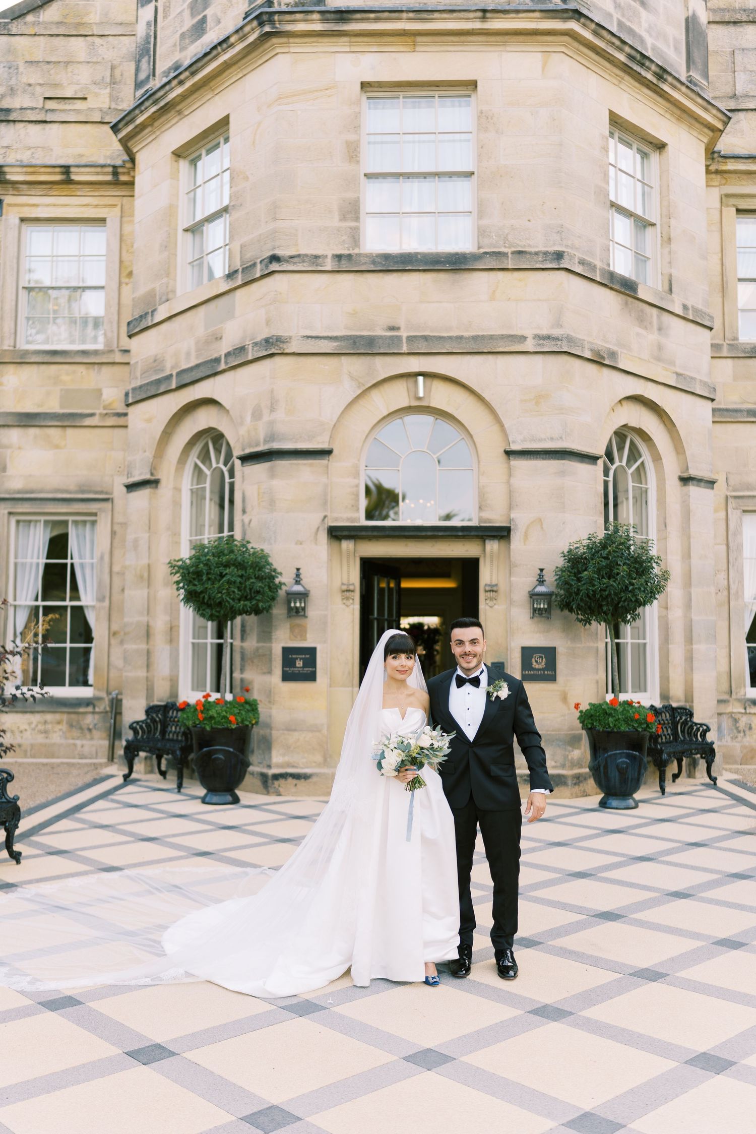 Bride and groom pose together in front of an elegant stone manor house on their wedding day.