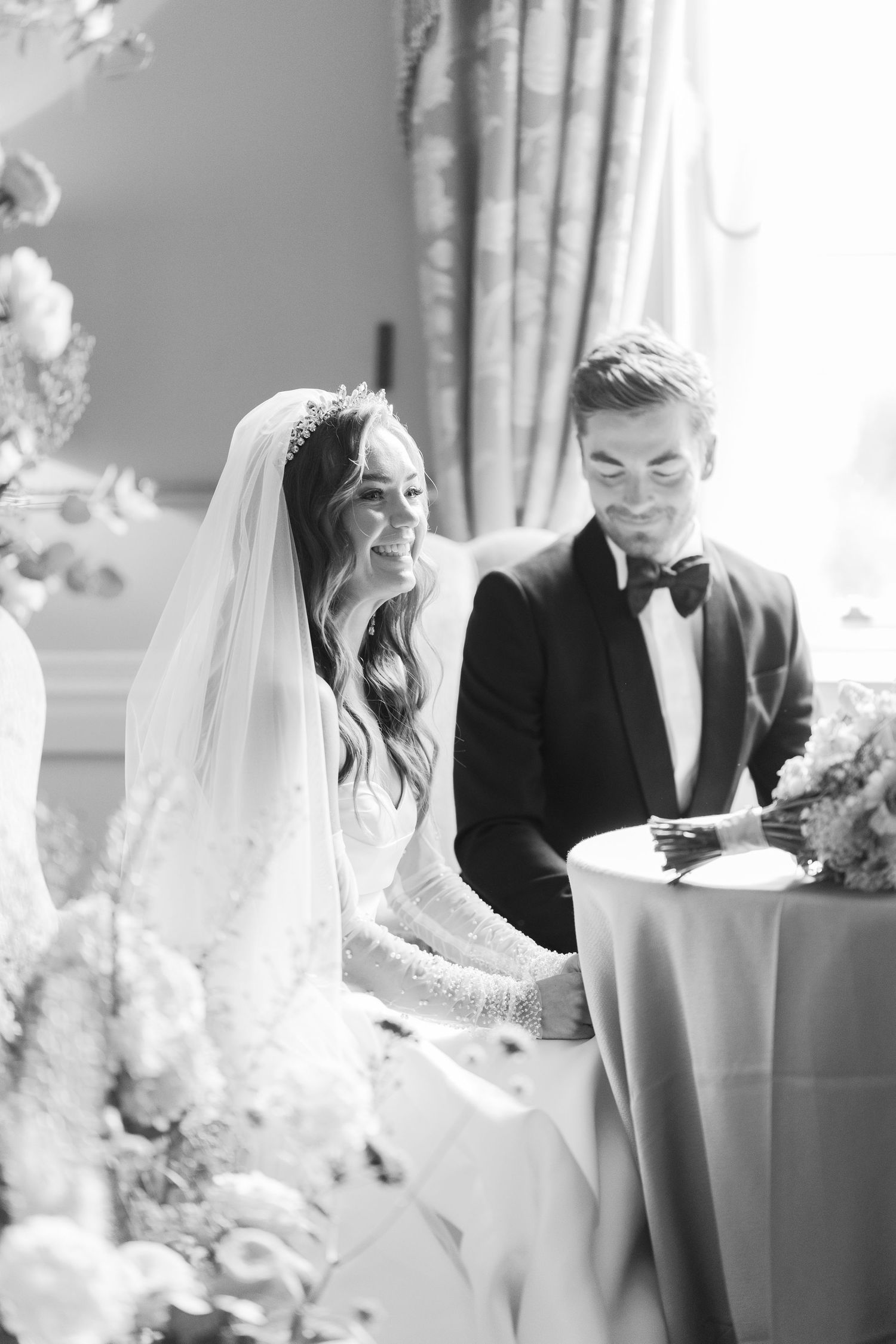 Smiling bride in tiara veil and groom in tuxedo sign wedding register at ceremony.
