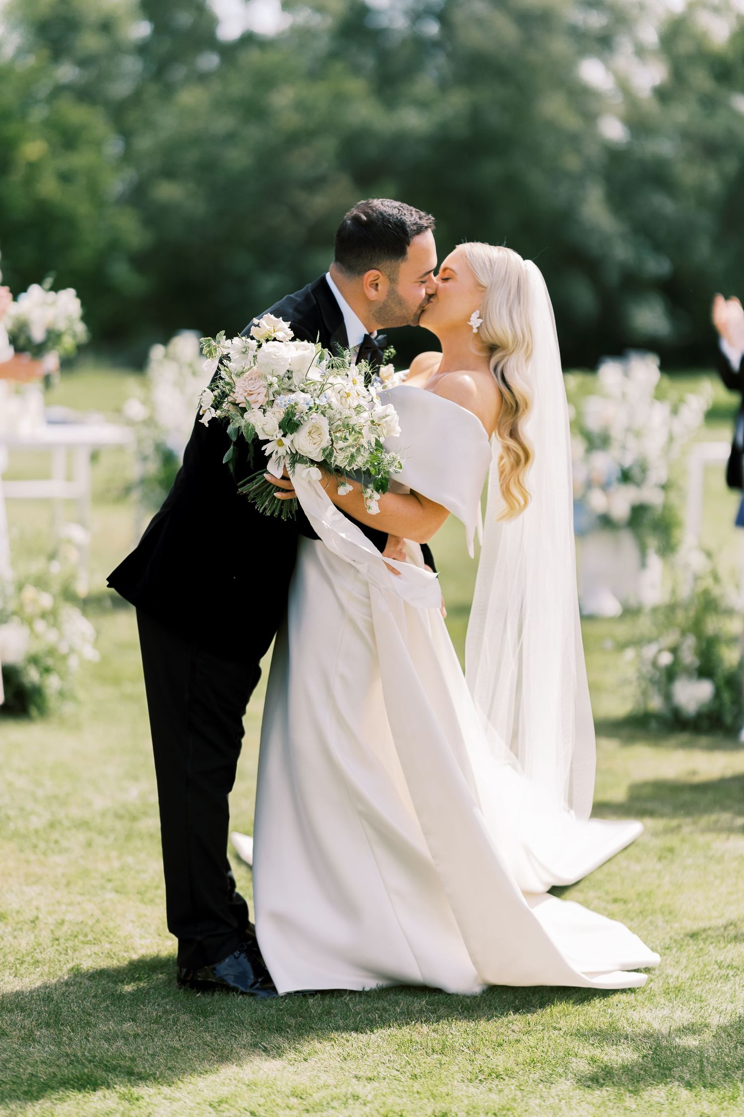 Bride and groom sharing first kiss on green lawn at outdoor wedding ceremony.