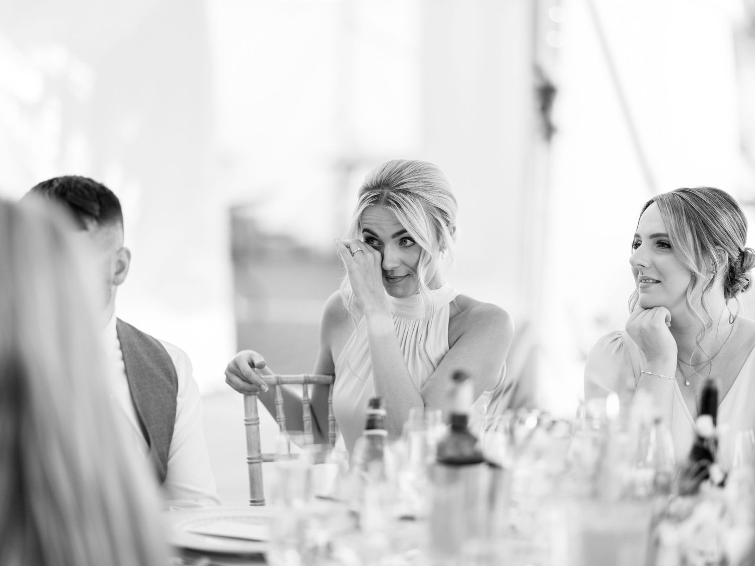 Emotional wedding guest wiping tears at reception table in black and white photo.
