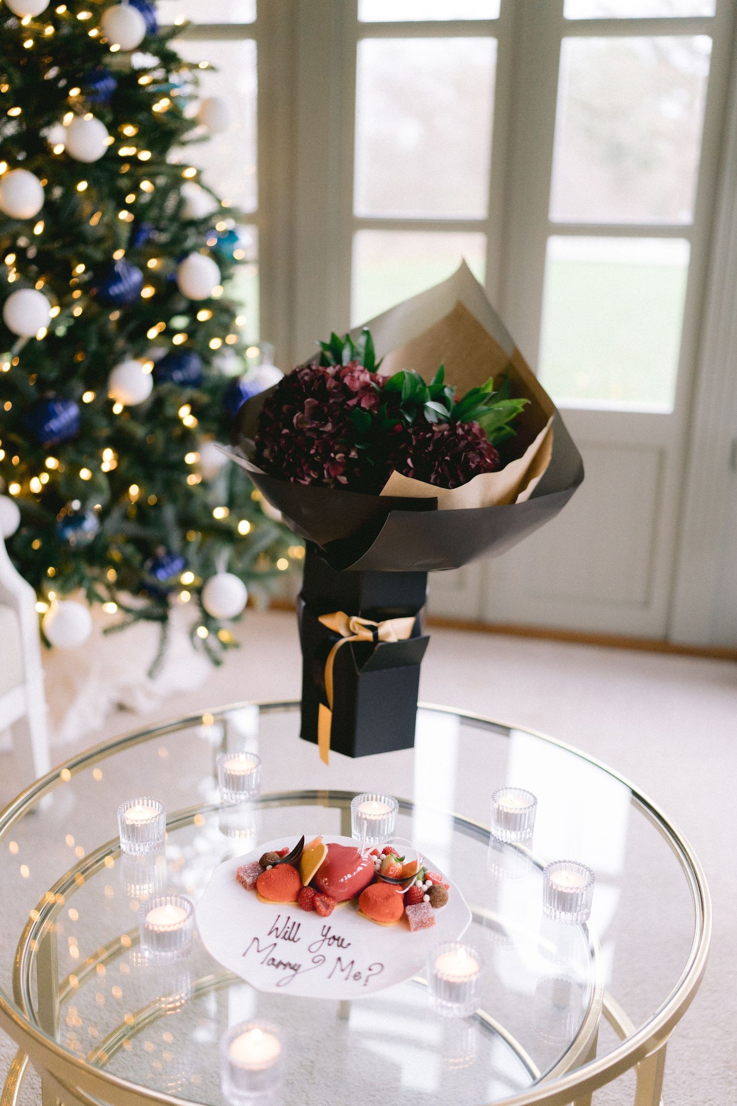 Romantic marriage proposal setup with bouquet, strawberries, candles and Will You Marry Me note.
