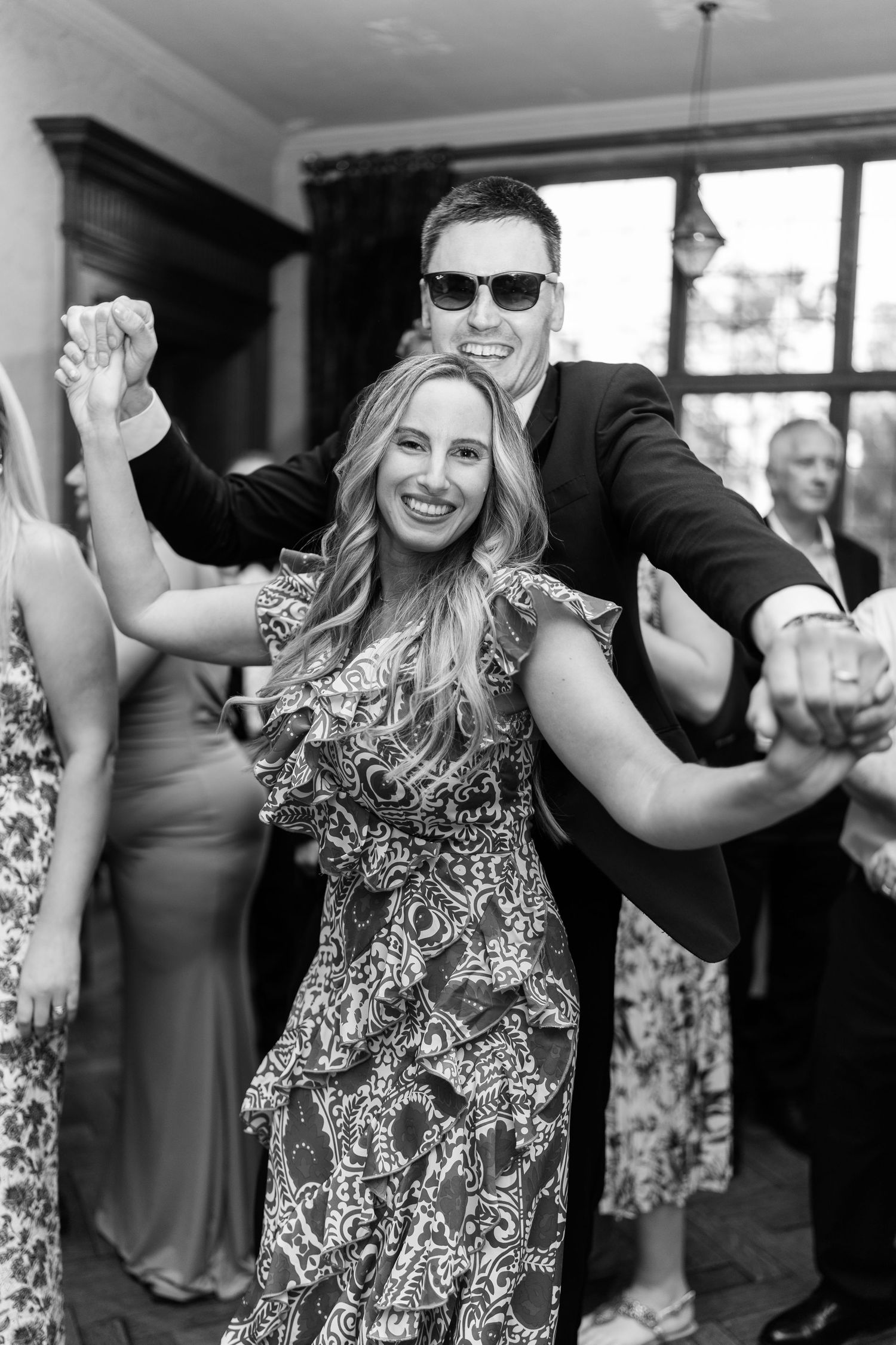 Joyful wedding guests dancing and celebrating on the dance floor in black and white photo.