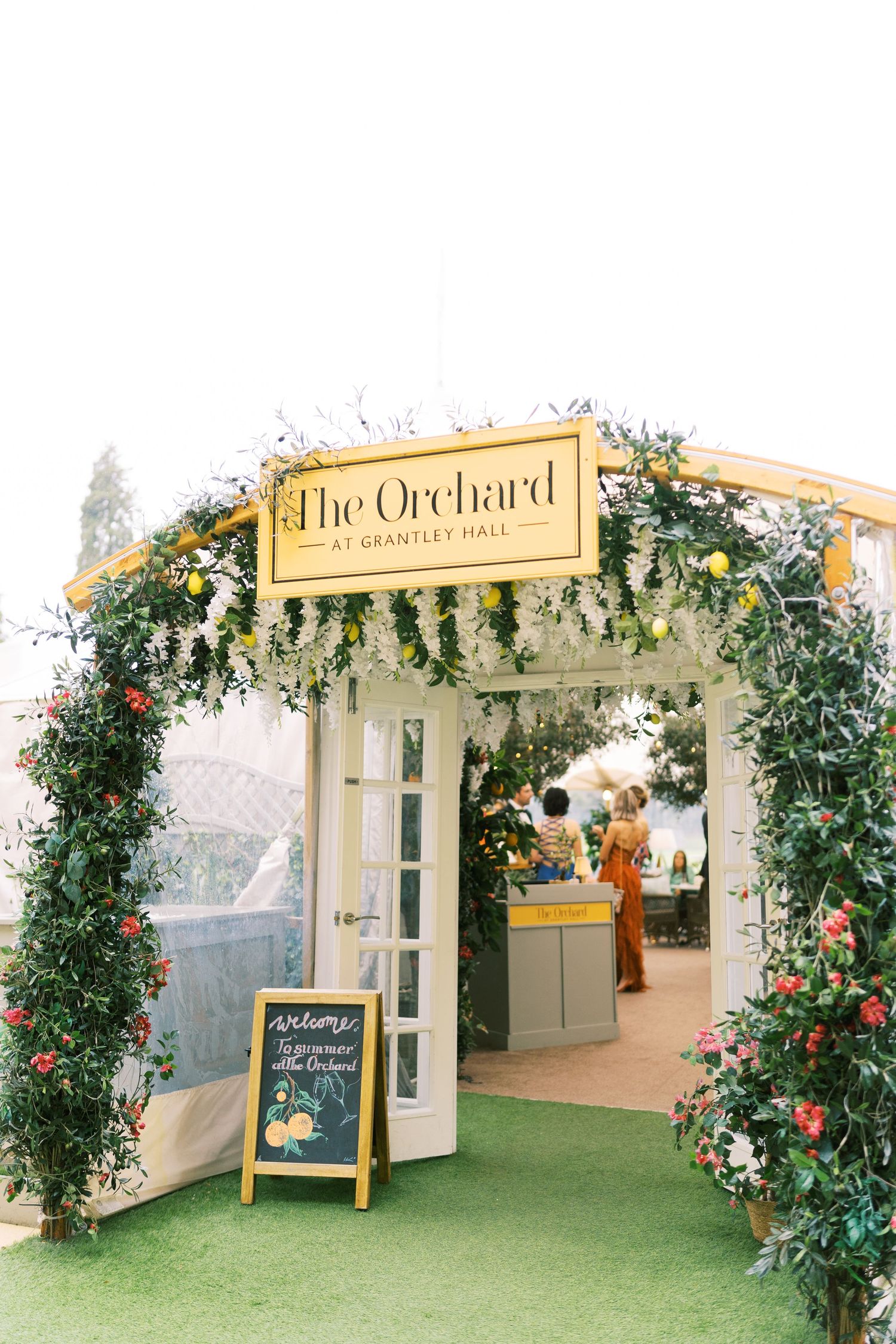 The Orchard at Grantley Hall entrance adorned with lush greenery, floral arch, and a welcome chalkboard sign.