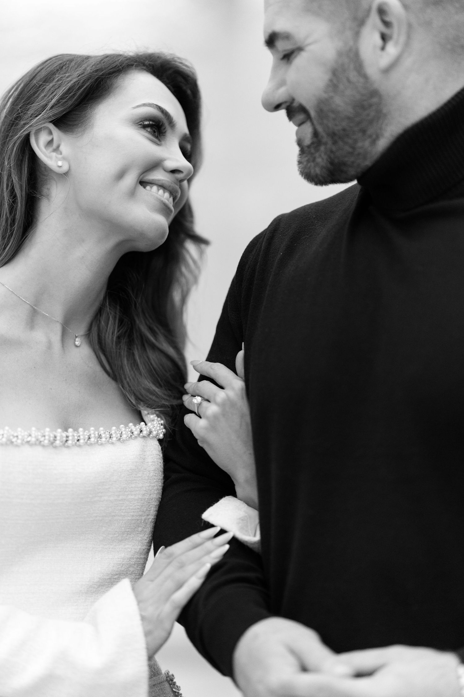 Black and white portrait of smiling engaged couple gazing at each other lovingly indoors.