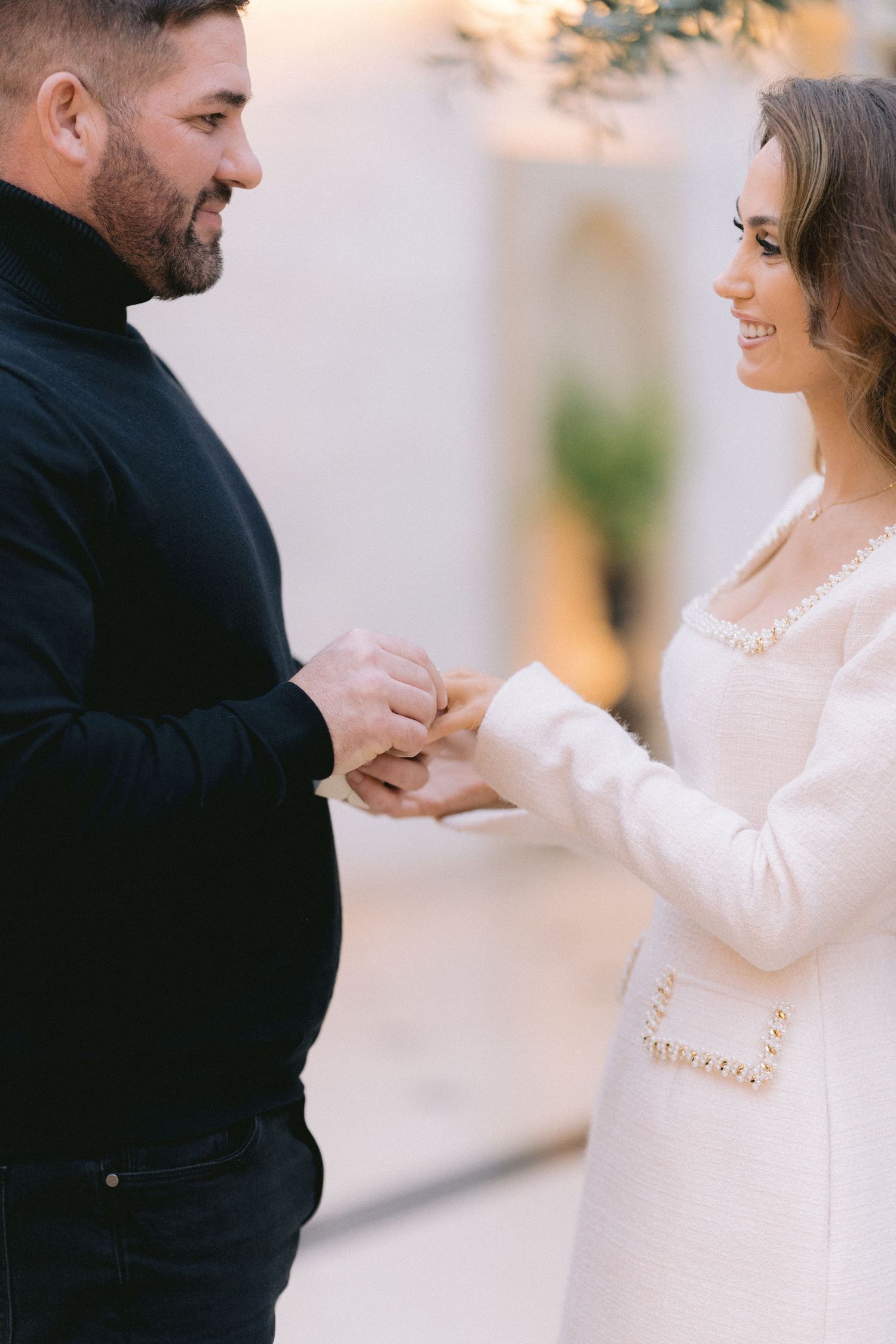 Couple sharing a tender moment holding hands during their engagement, woman in white dress smiling joyfully.