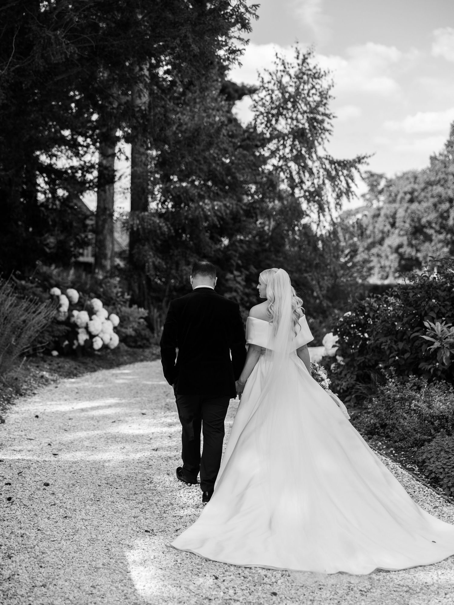 Bride and groom walking hand in hand down a garden path in black and white wedding photo.