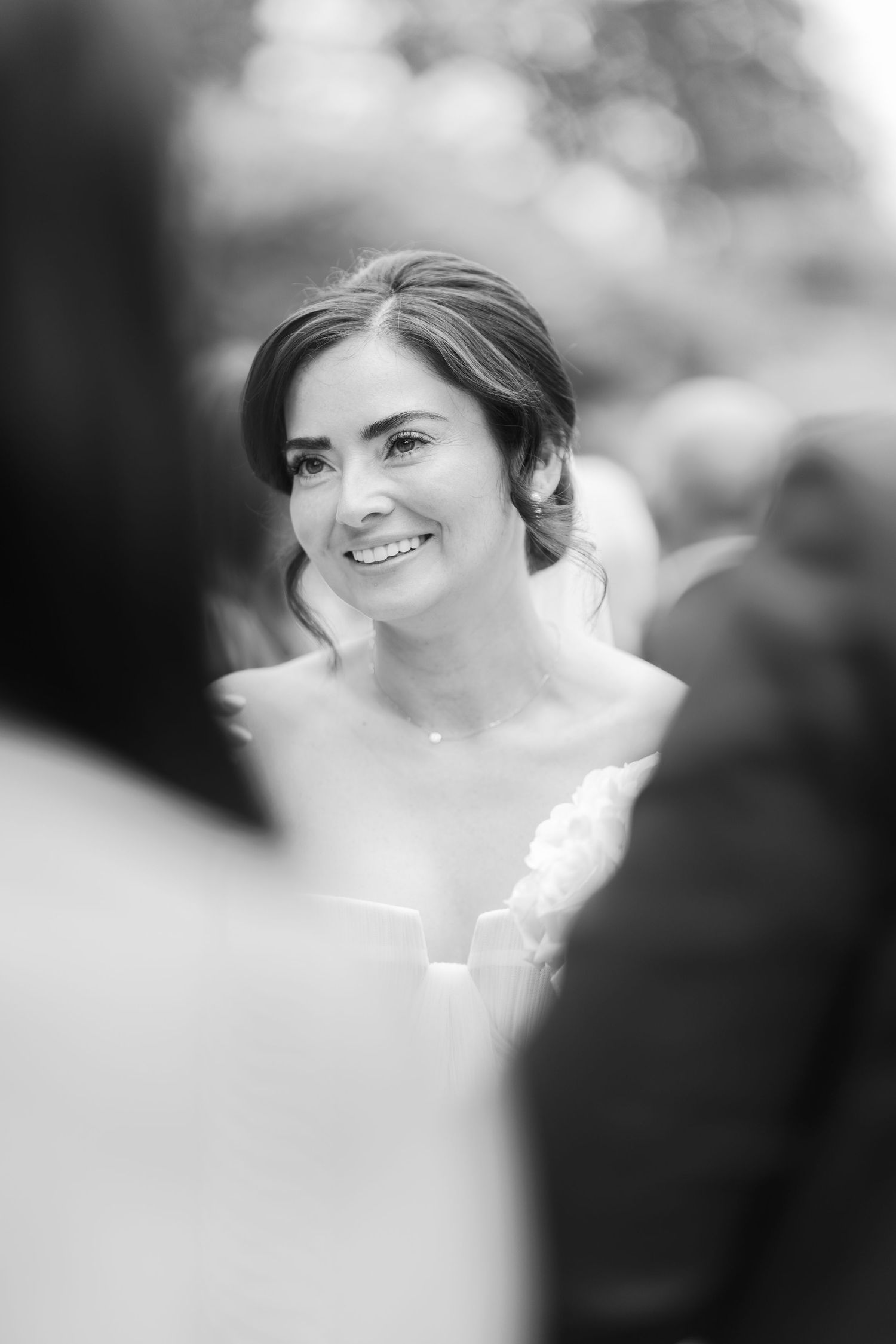 Black and white photo of a smiling bride in a strapless gown during her outdoor wedding ceremony.