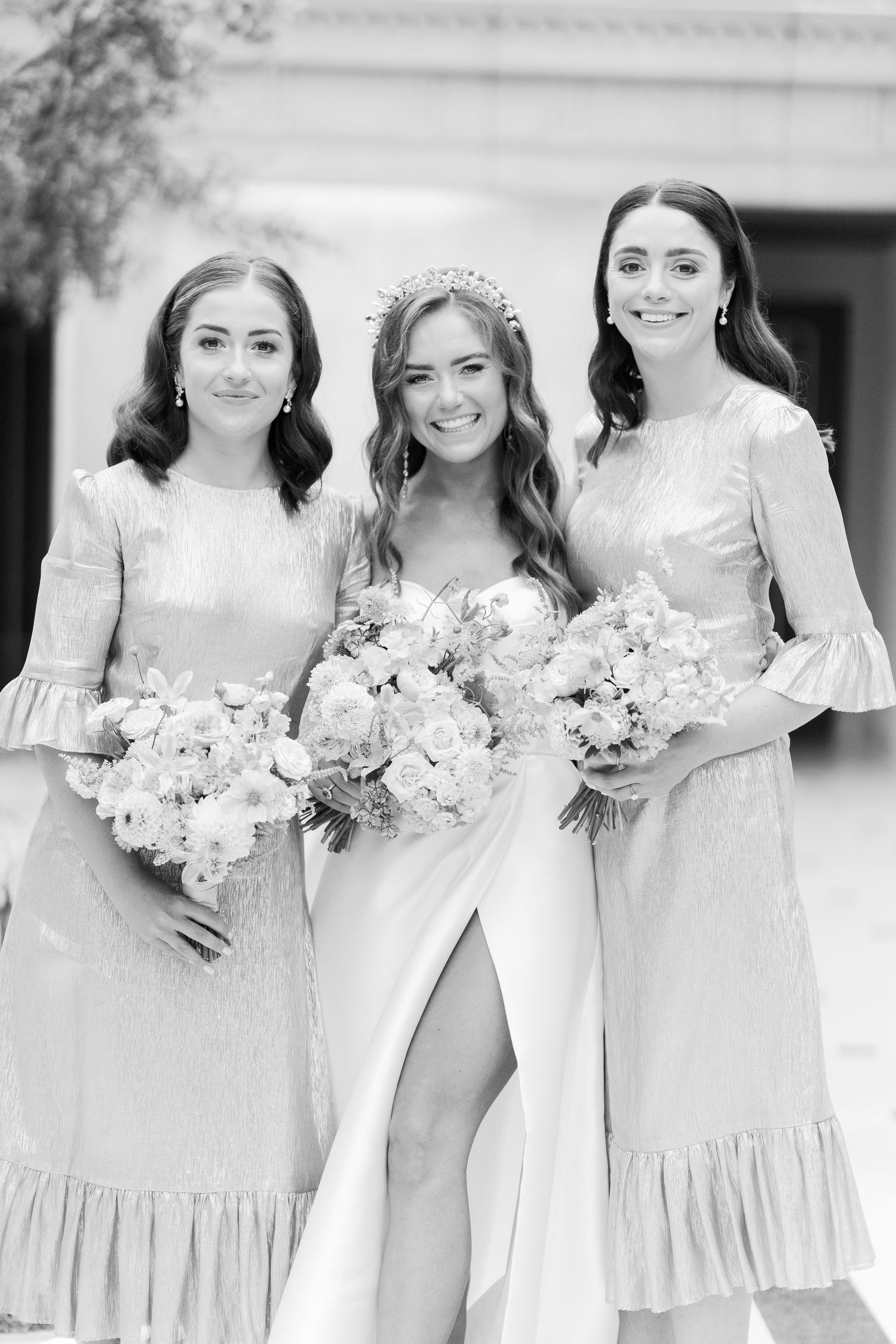 Black and white photo of bride wearing tiara flanked by two bridesmaids holding floral bouquets.