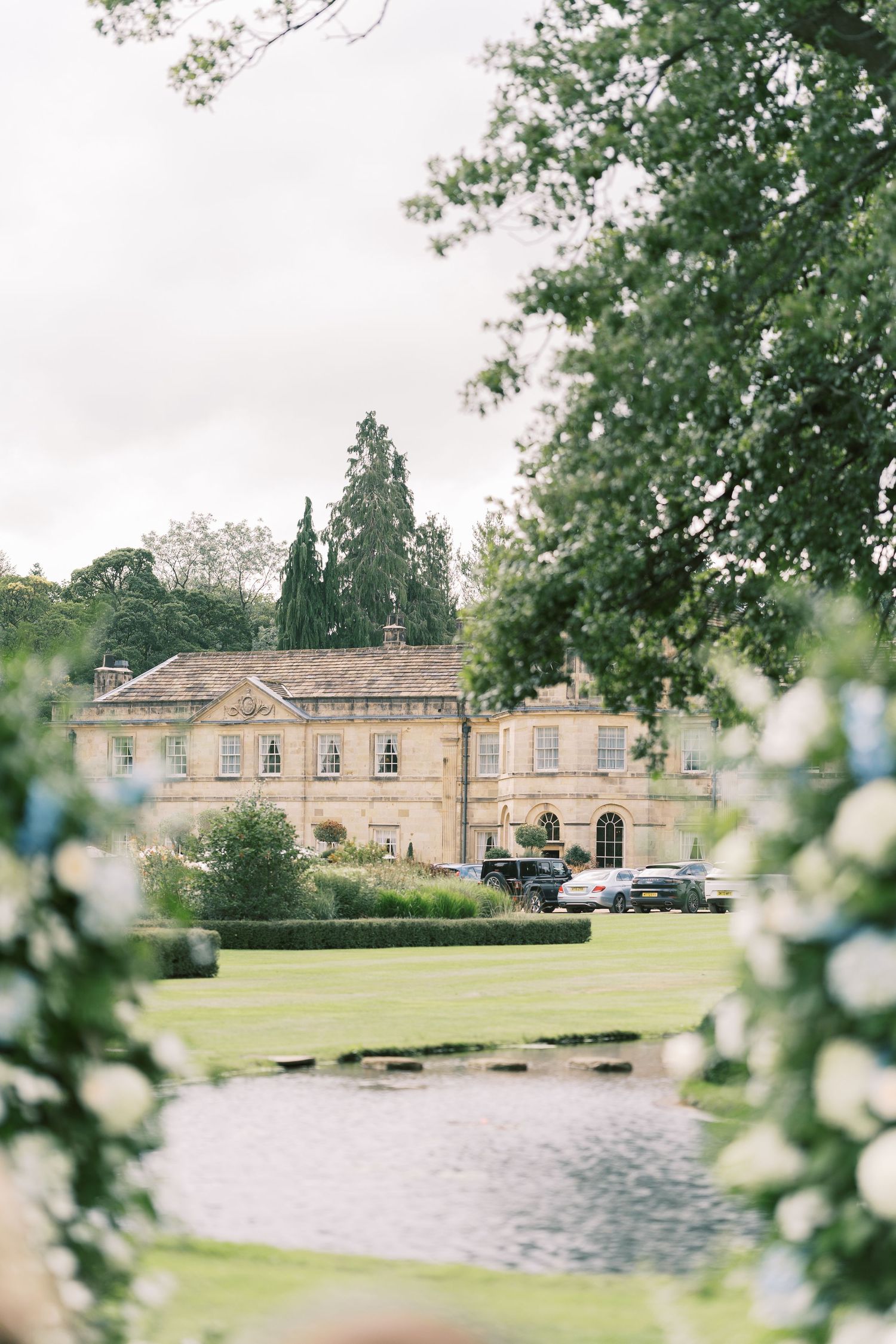 Elegant Georgian country house wedding venue with manicured lawns and a tranquil pond, framed by lush green trees.