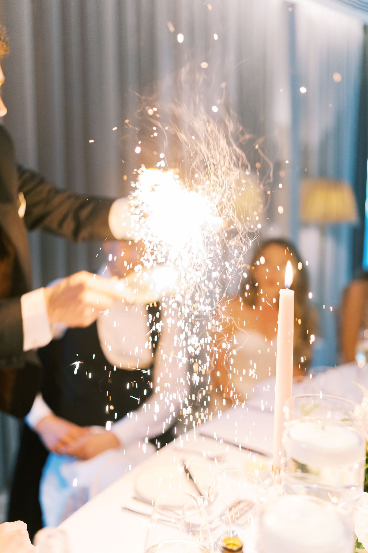 Rice being thrown at a wedding reception dinner table with candles and glassware, creating a festive celebratory moment.