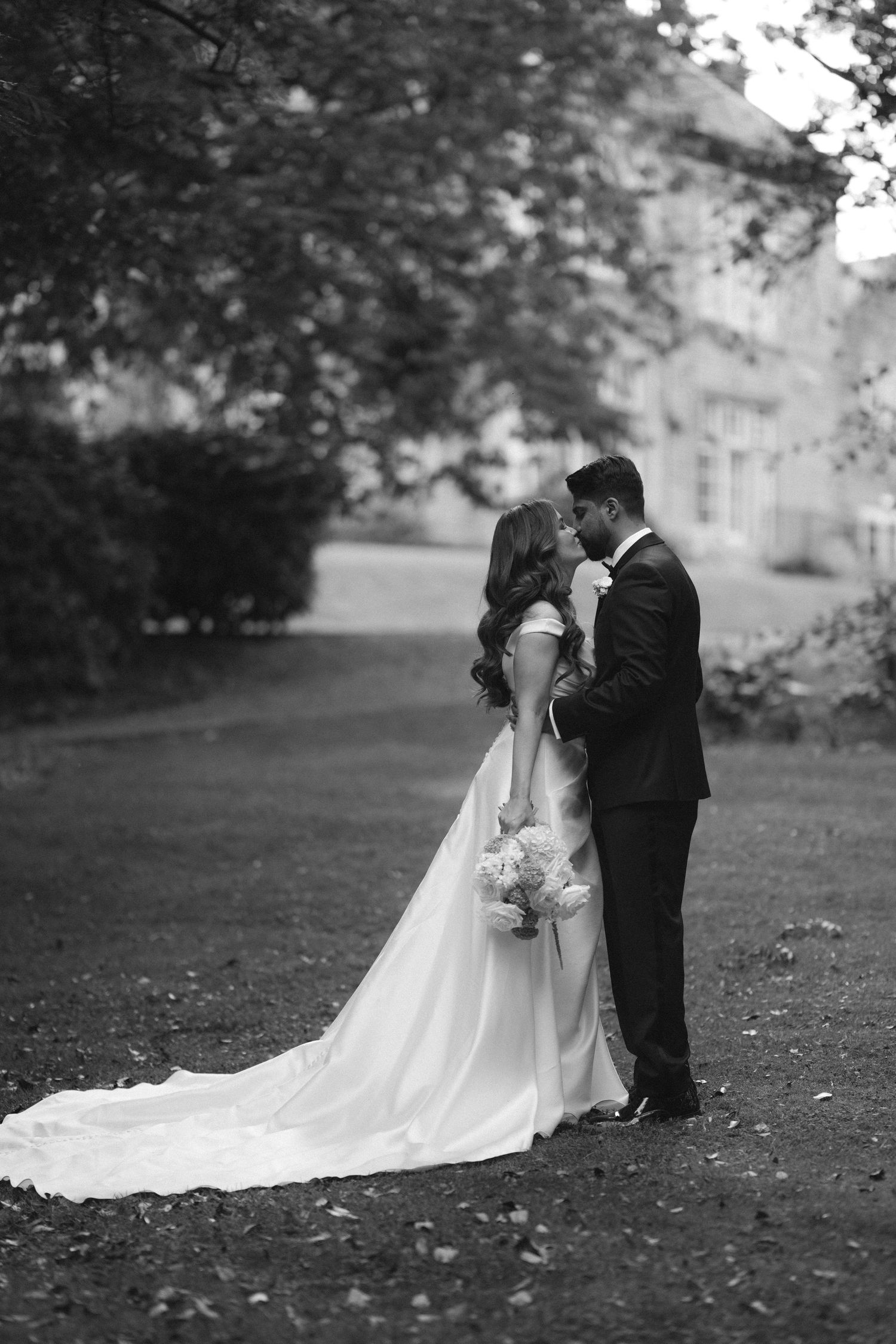 Black and white photo of a bride and groom sharing an intimate moment in a garden, with a flowing wedding dress train.