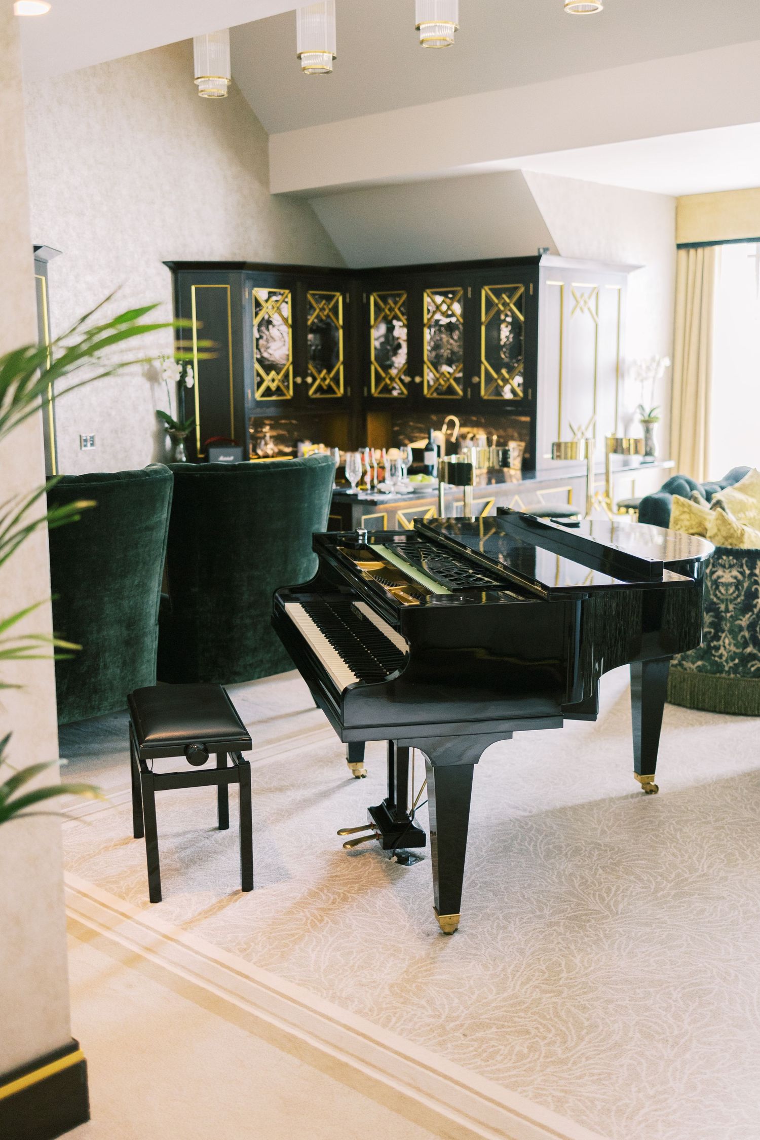 Elegant living room with a black grand piano, green velvet sofa, and ornate dark cabinet with gold accents.