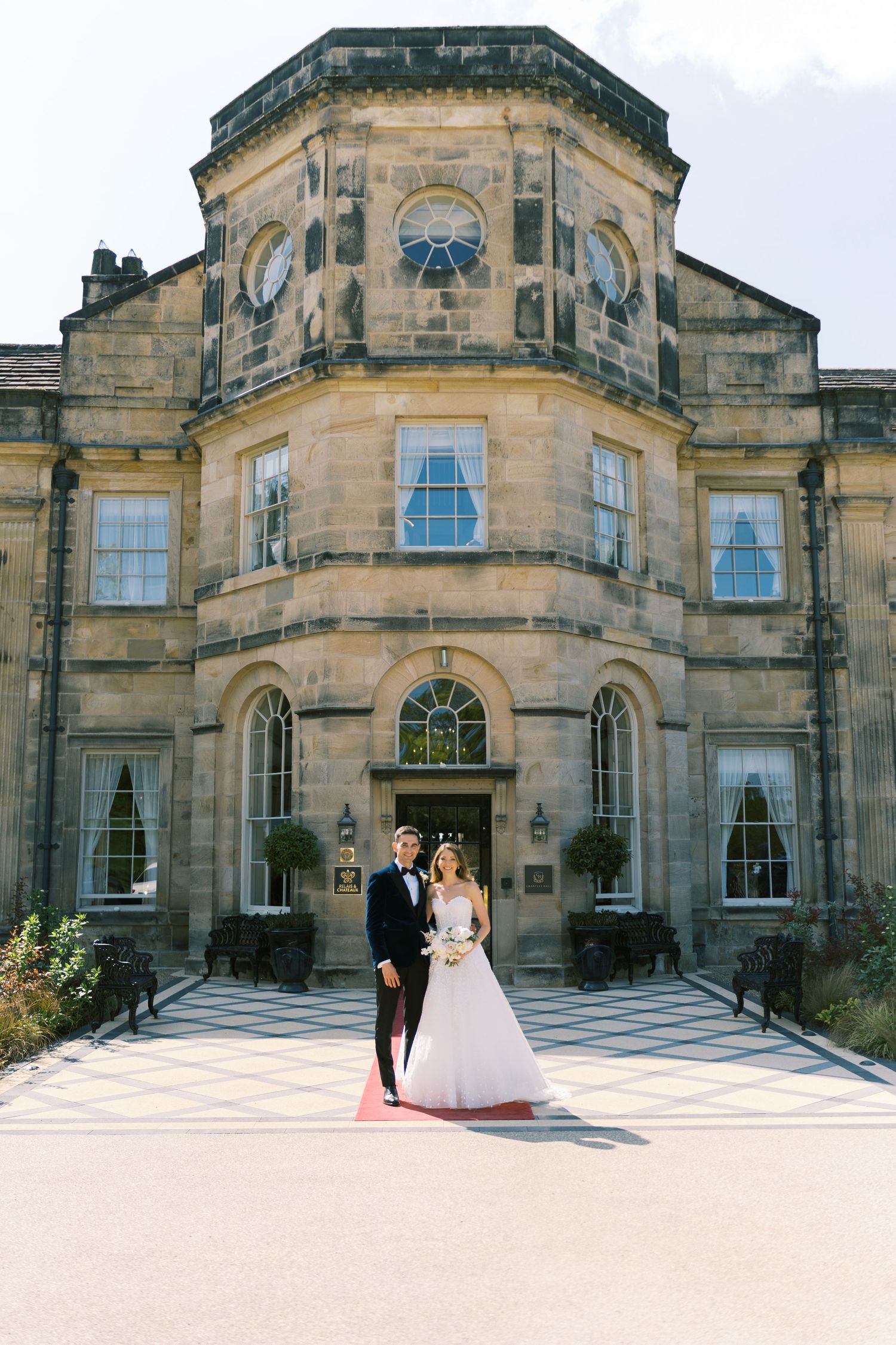 Bride and groom pose before a grand Georgian stone manor house on their wedding day.
