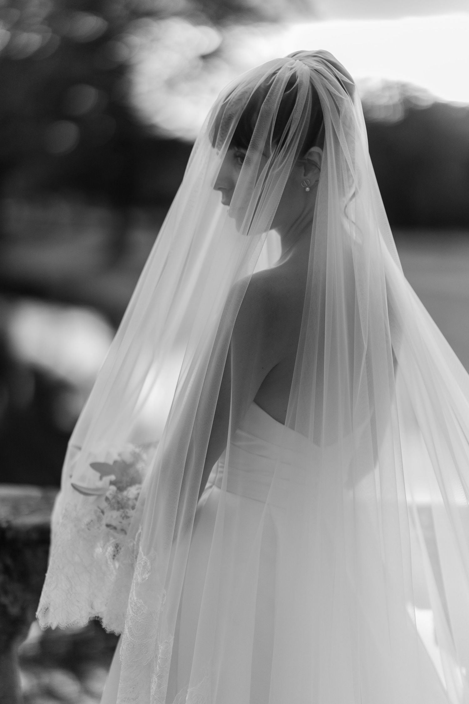 Elegant bride in a white wedding gown and flowing veil, captured in a timeless black and white portrait.