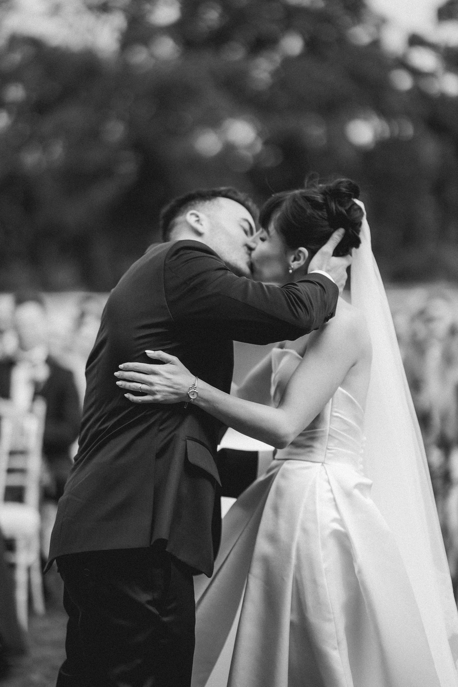 Bride and groom share first kiss at outdoor wedding ceremony in black and white photo.