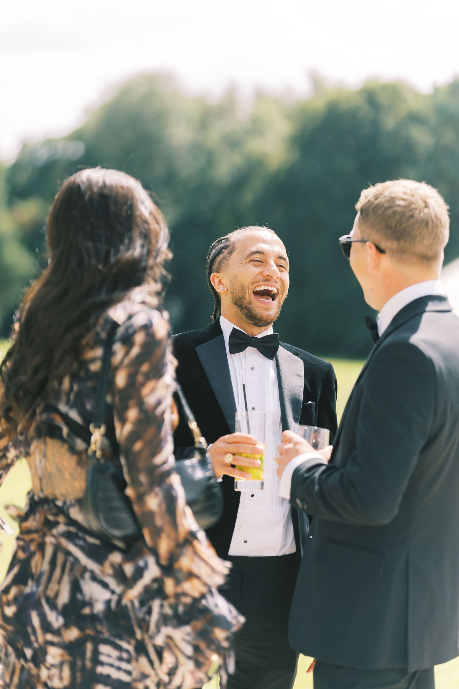 Guests in formal attire laughing and socializing outdoors at an elegant event, holding champagne glasses.