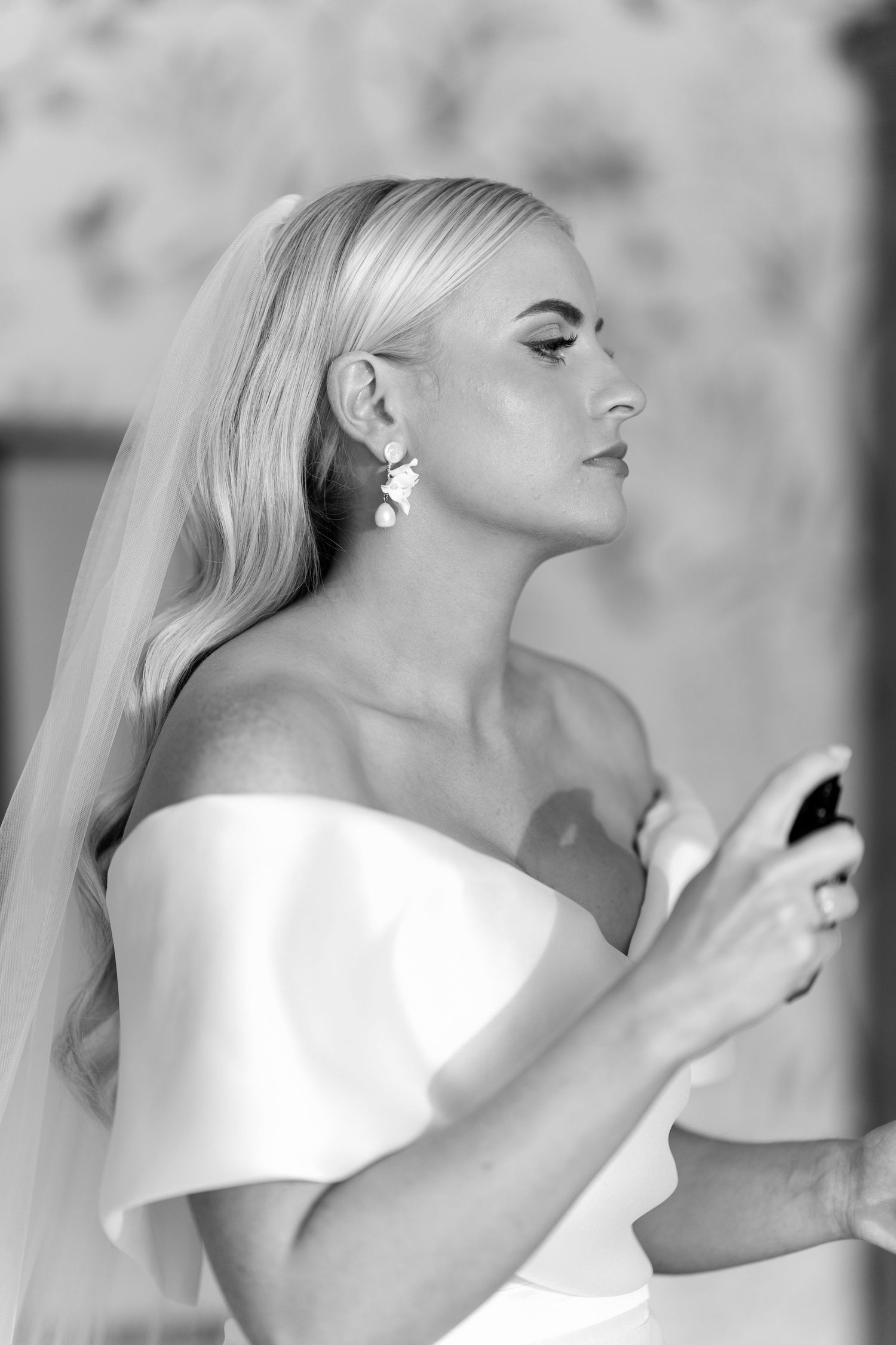 Black and white profile portrait of blonde bride in off-shoulder gown wearing statement drop earrings.