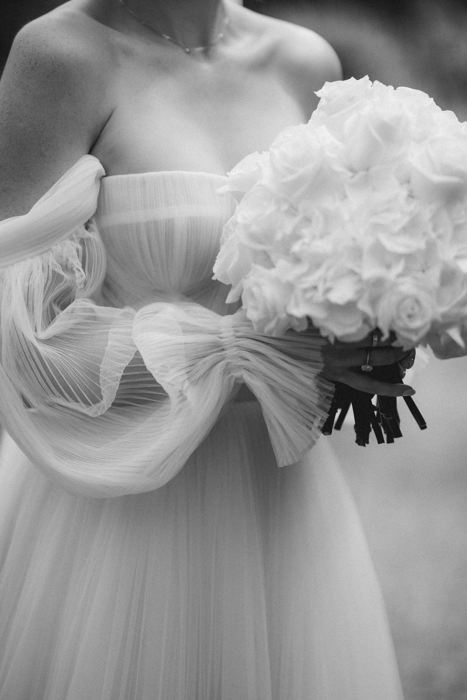 Black and white photo of a bride in a tulle gown holding a white rose and hydrangea bouquet.