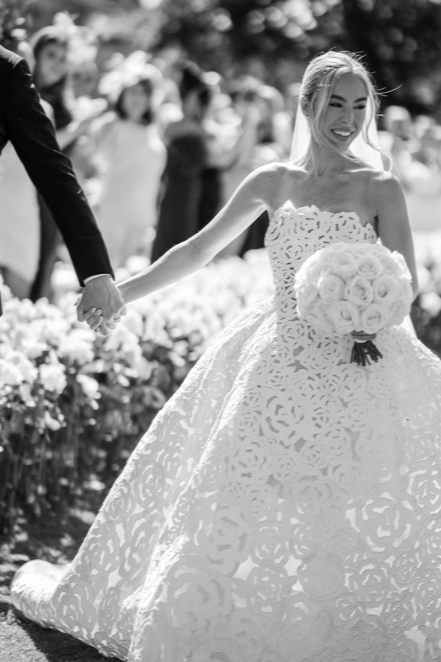 Black and white photo of joyful bride in ornate lace ball gown holding bouquet.