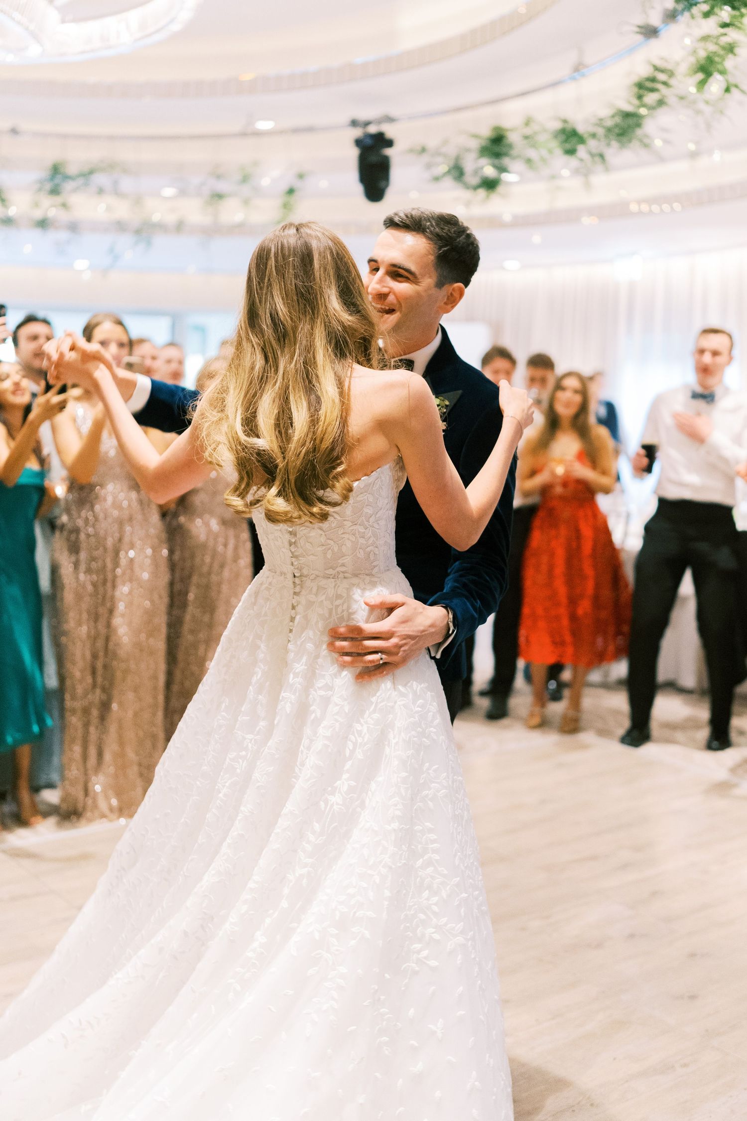 Bride and groom share their first dance at elegant wedding reception while guests applaud in background.