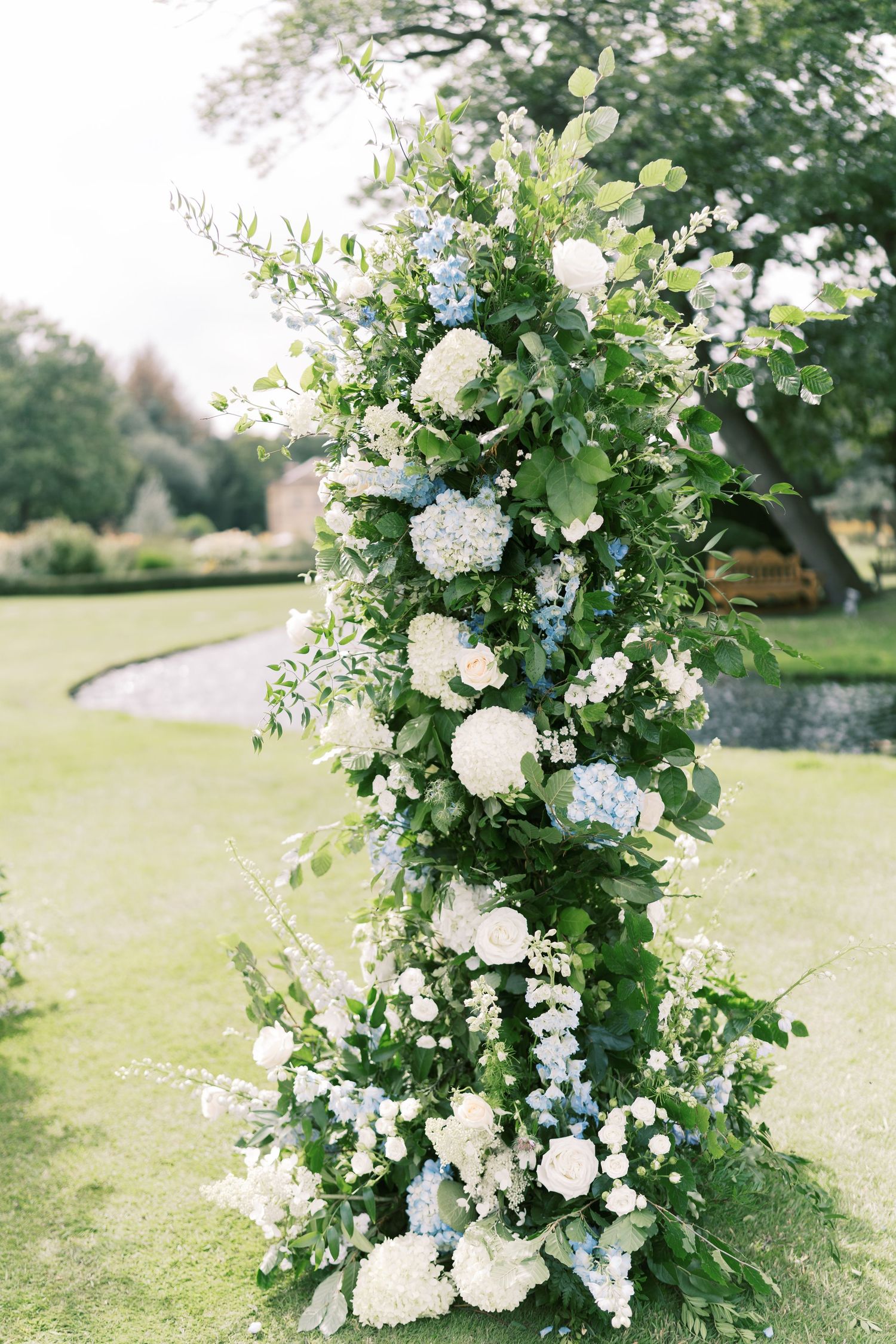 Lush wedding arch column adorned with white hydrangeas, blue flowers, and green foliage for outdoor ceremony.