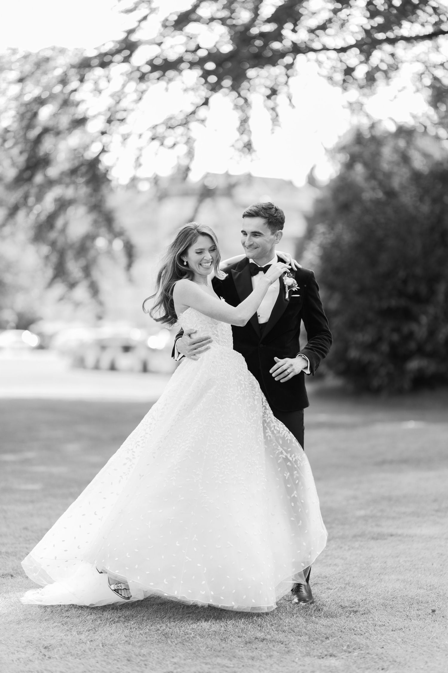 Black and white photo of a bride and groom dancing outdoors, smiling joyfully on their wedding day.
