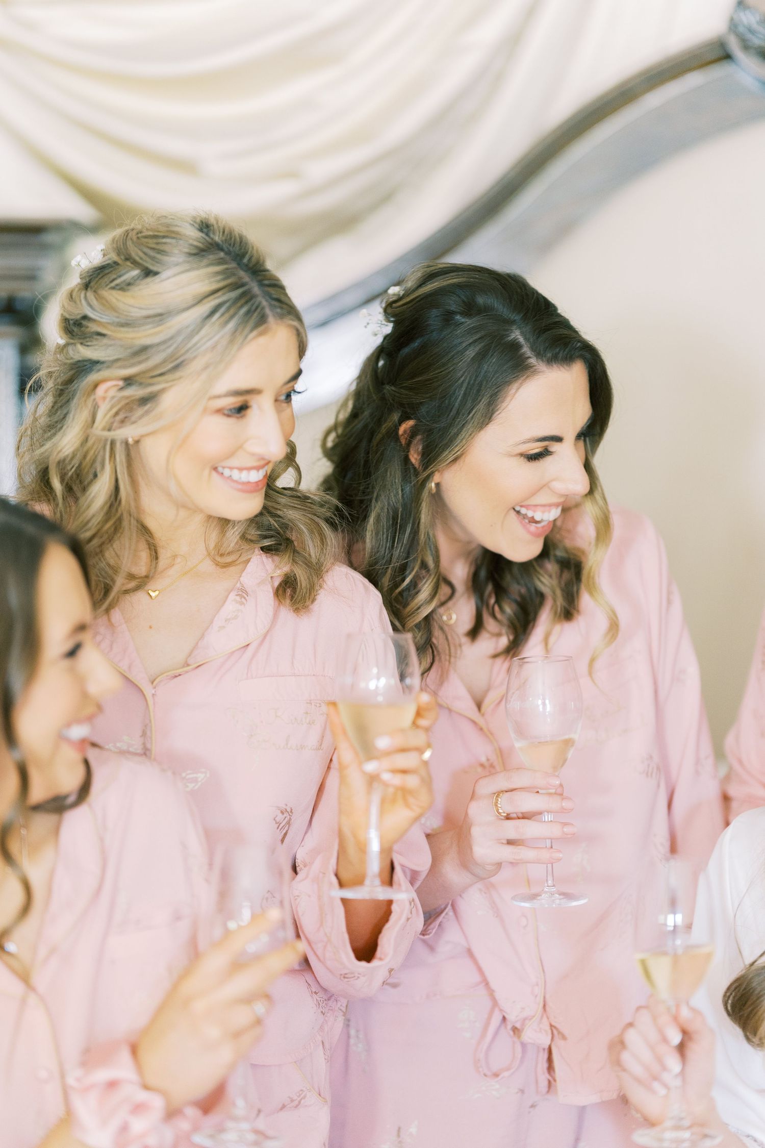 Bridesmaids in pink robes toasting with champagne glasses, smiling and celebrating together before a wedding.
