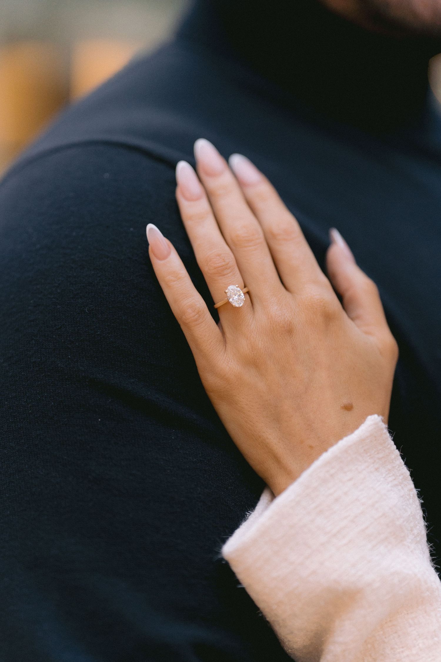 Close-up of a stunning pear-shaped diamond engagement ring on woman's hand against black turtleneck.