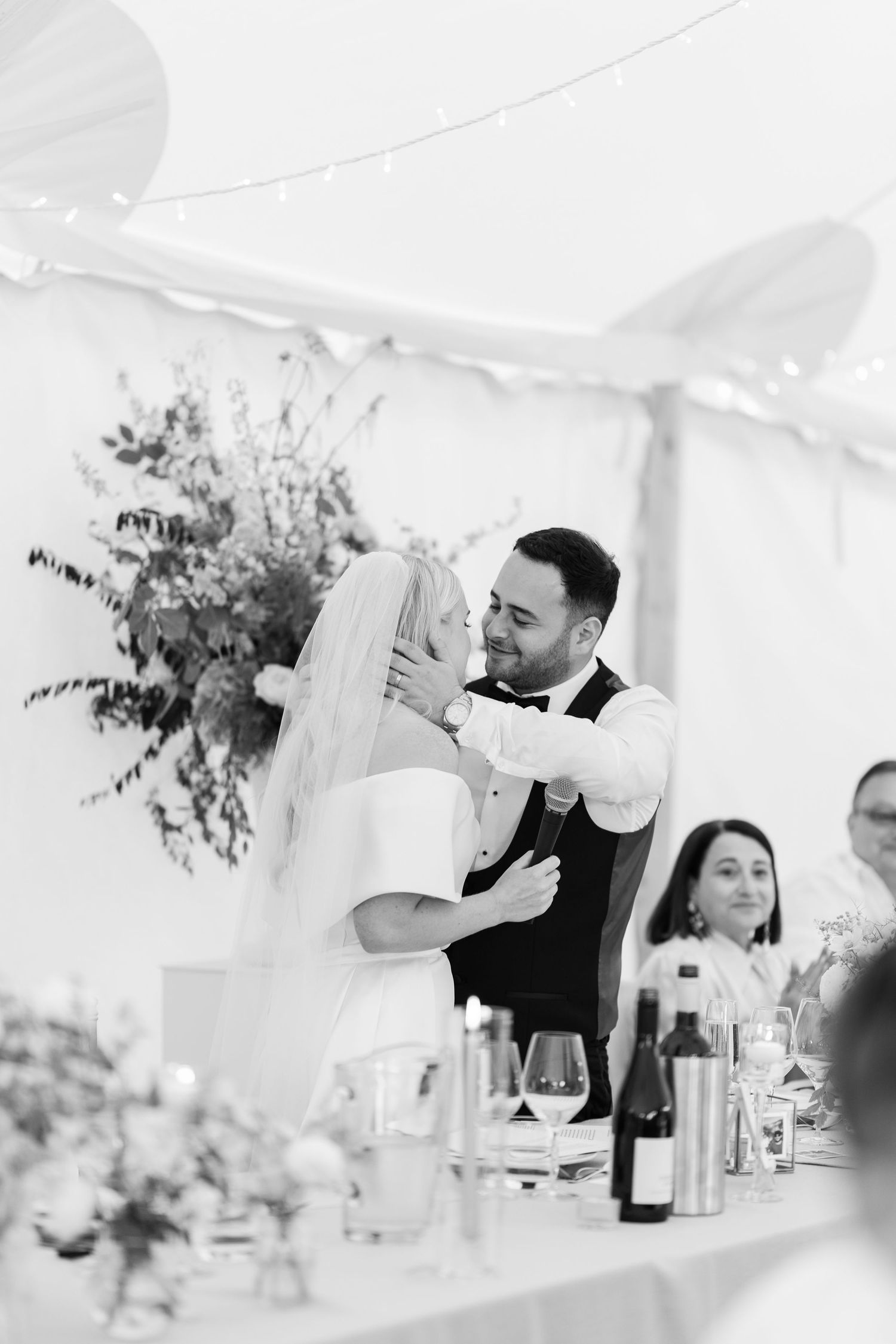 Bride and groom sharing a tender embrace during first dance at elegant tented wedding reception.