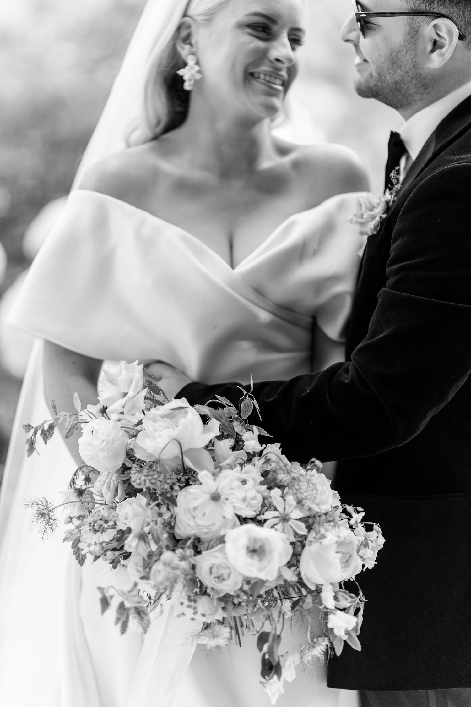 Black and white photo of bride and groom embracing, bride holding elegant floral bouquet.