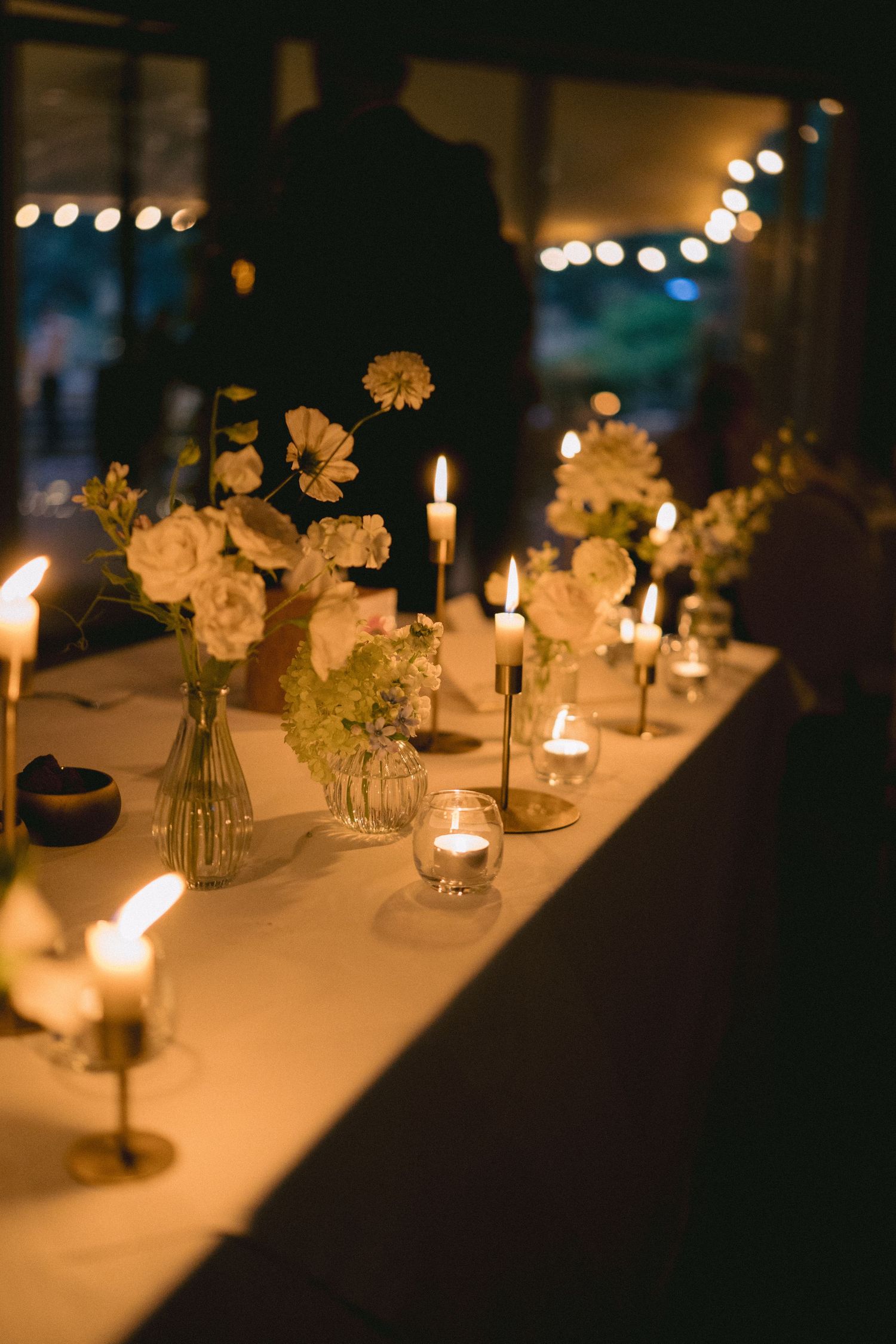 Elegant wedding reception table with white floral arrangements and glowing candles in warm candlelight.