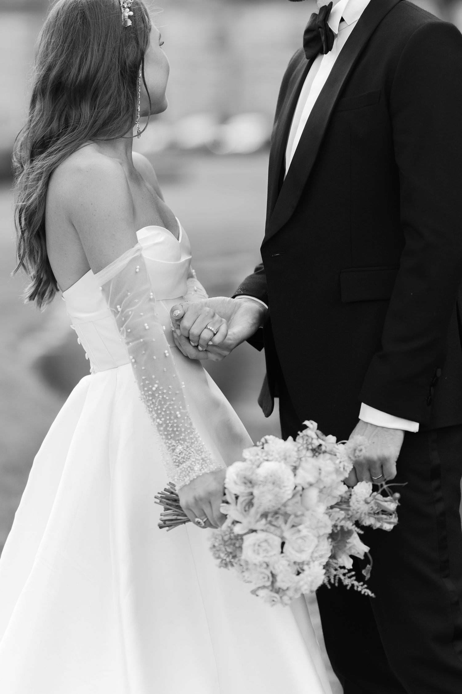 Black and white photo of bride in off-shoulder gown holding bouquet with groom in tuxedo on wedding day.