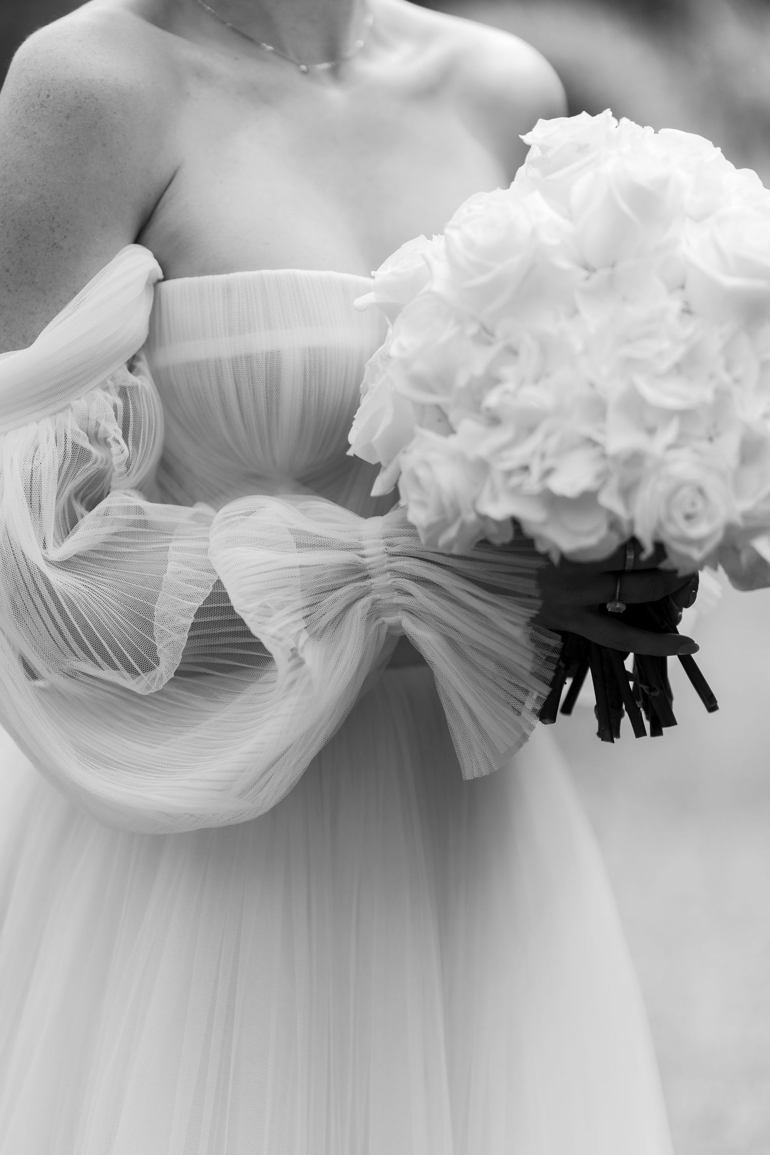 Black and white photo of bride in off-shoulder tulle wedding gown holding lush white hydrangea bouquet.
