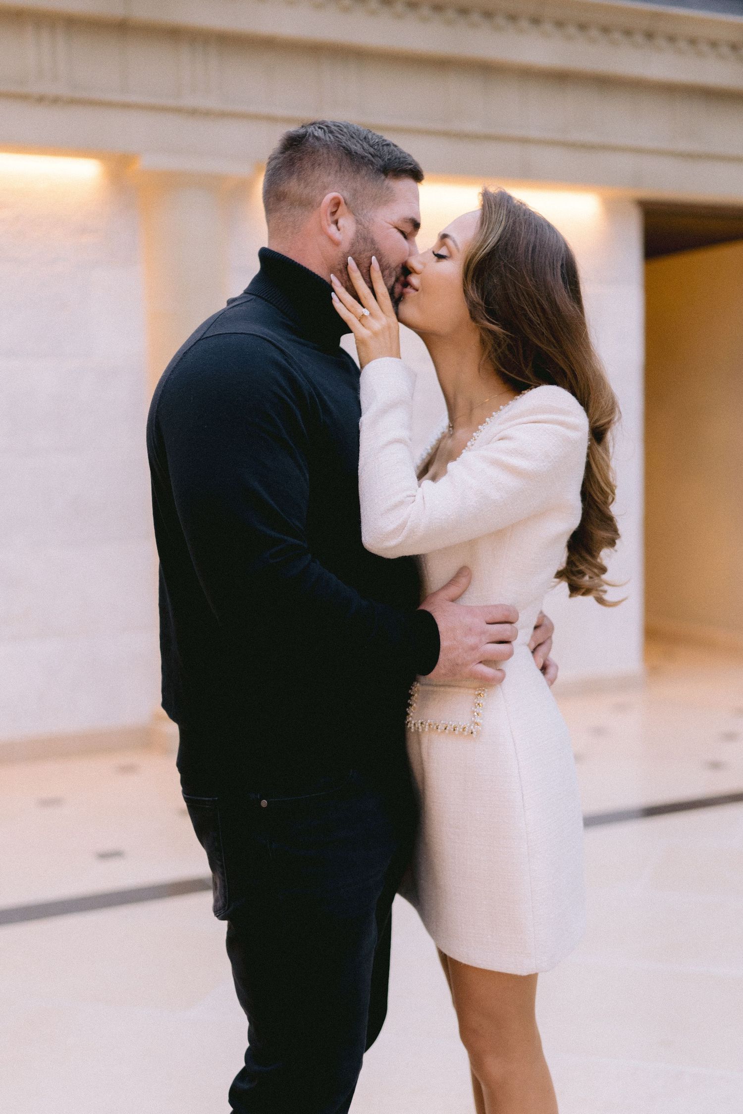 Happy couple kissing during their engagement photoshoot inside a grand architectural building.
