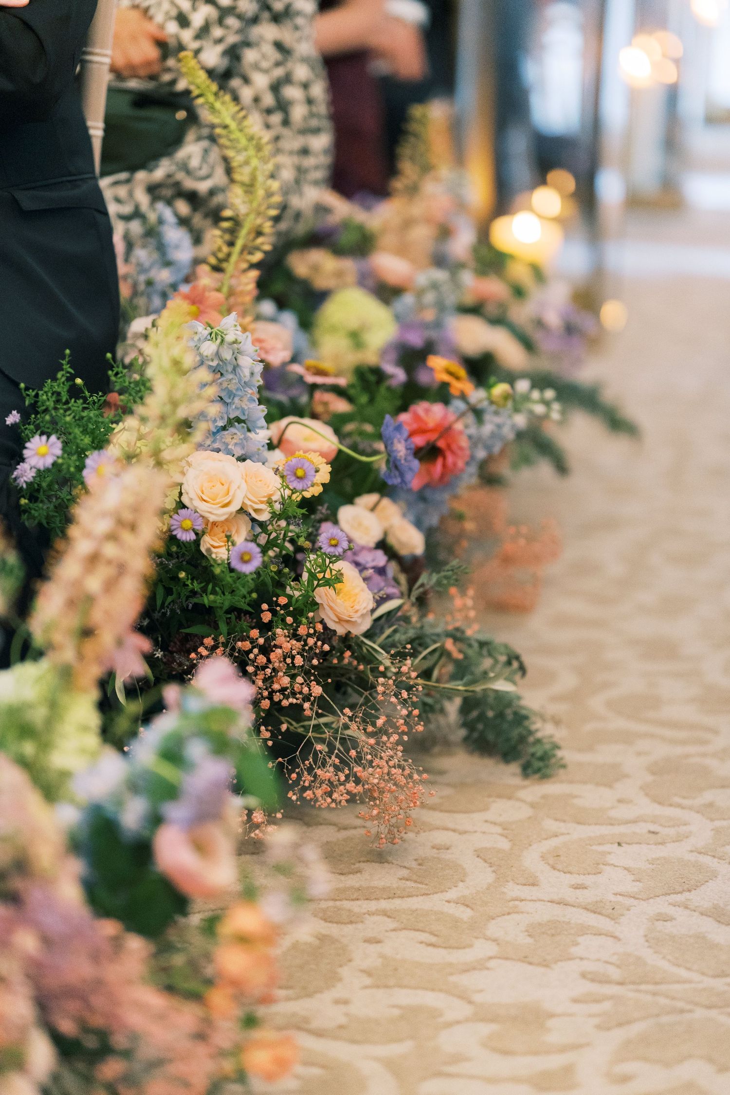 Colorful wedding floral arrangements with roses, wildflowers, and greenery lining a decorated table at an elegant reception.