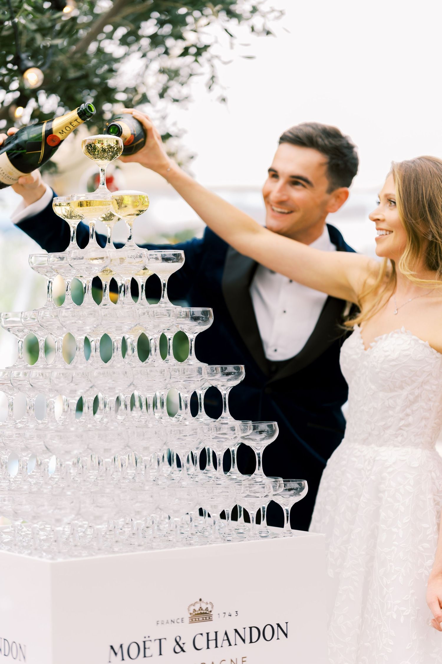 Bride and groom pouring Moet & Chandon champagne tower at elegant wedding reception celebration.