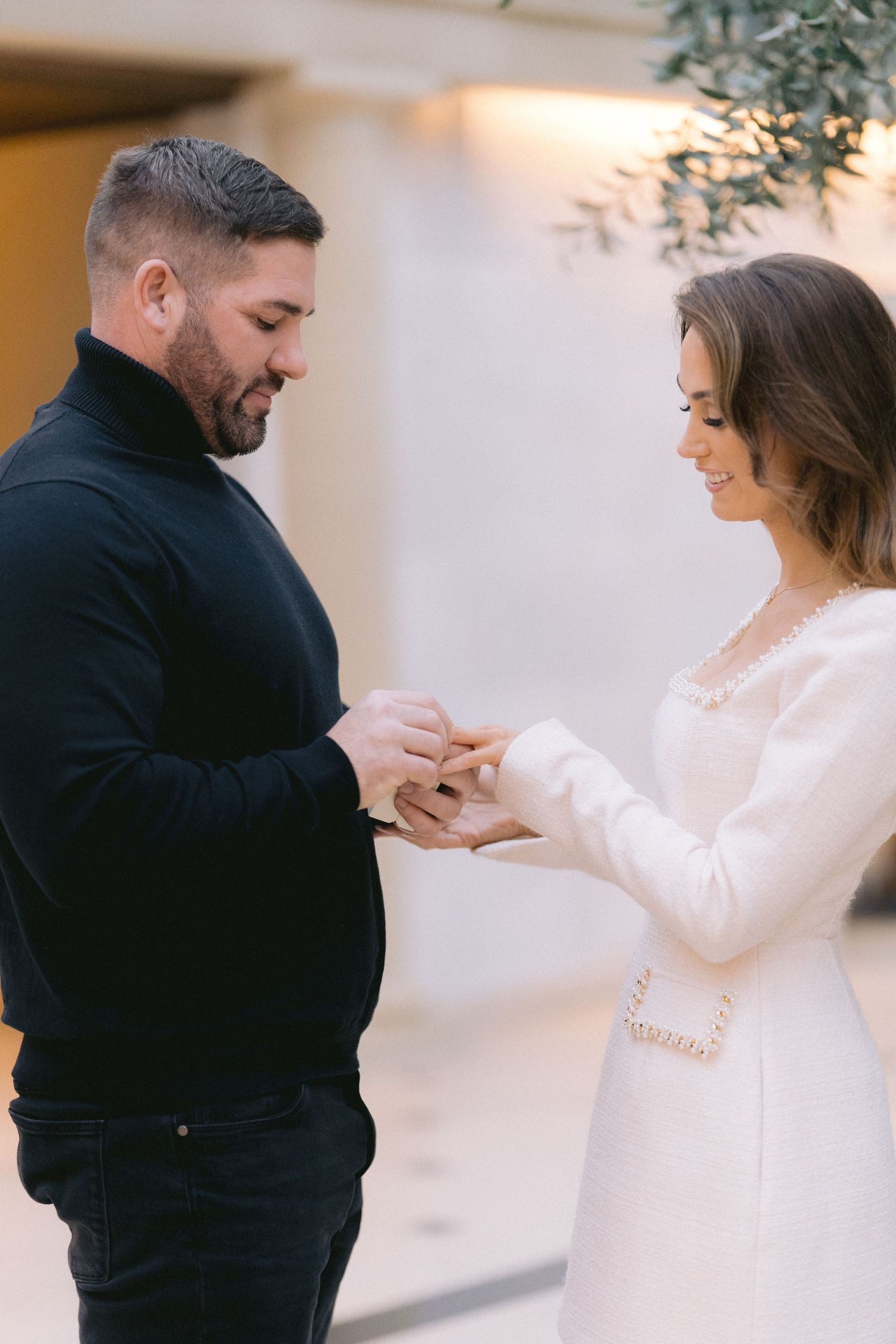 Man placing engagement ring on smiling womans finger during intimate proposal moment indoors.