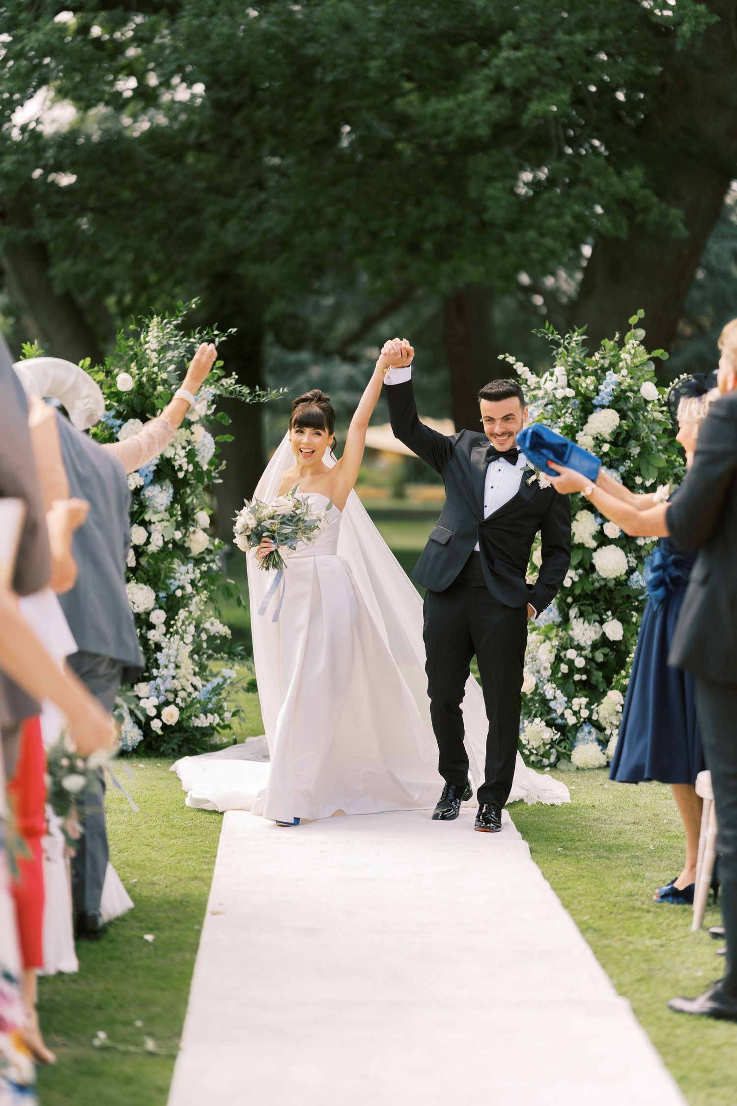 Newlyweds raise hands in celebration as they walk back down the aisle after outdoor garden wedding ceremony.