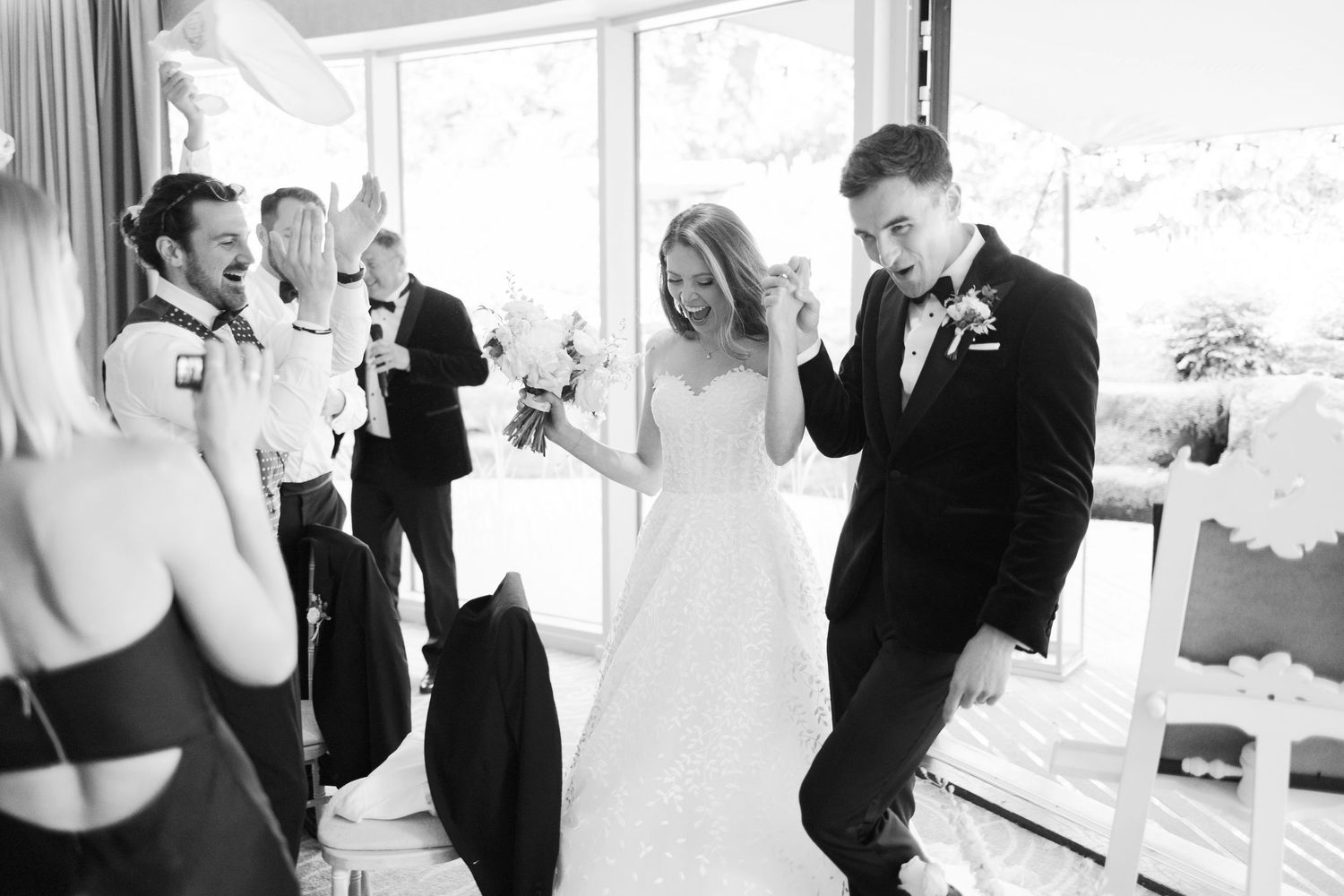 Joyful newlyweds dance with guests during black and white wedding reception celebration.