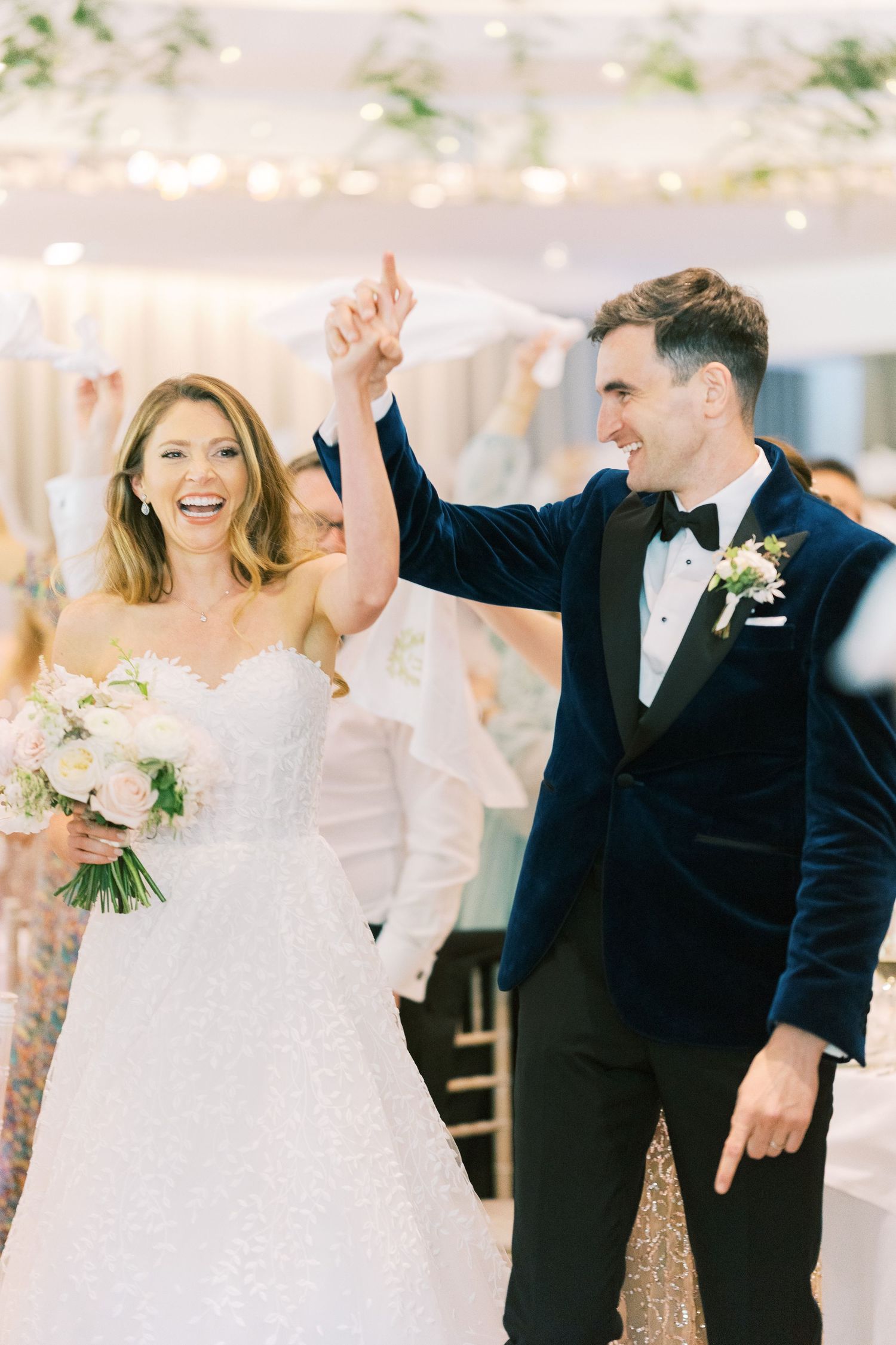 Smiling bride and groom in blue velvet tuxedo make grand entrance at elegant wedding reception.