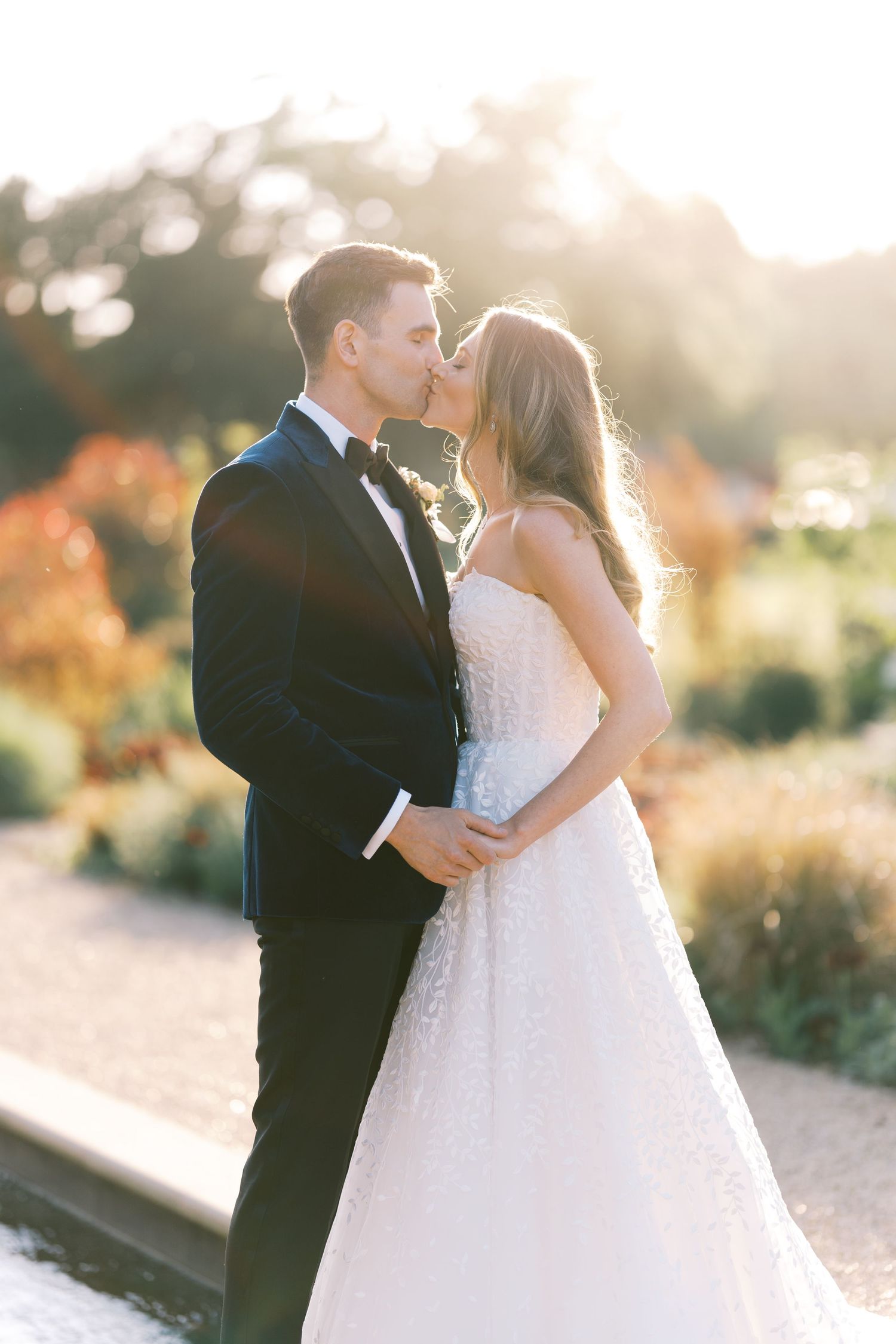 Bride and groom share a golden hour kiss in lush garden surroundings at their outdoor wedding.