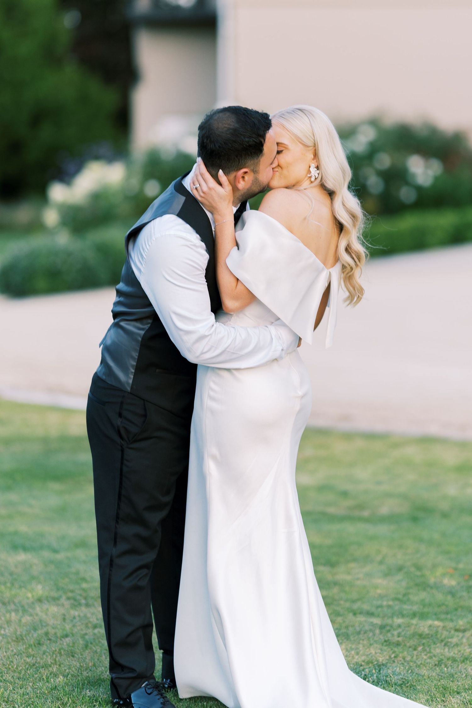 Bride and groom sharing a romantic kiss on a lawn in golden evening light.